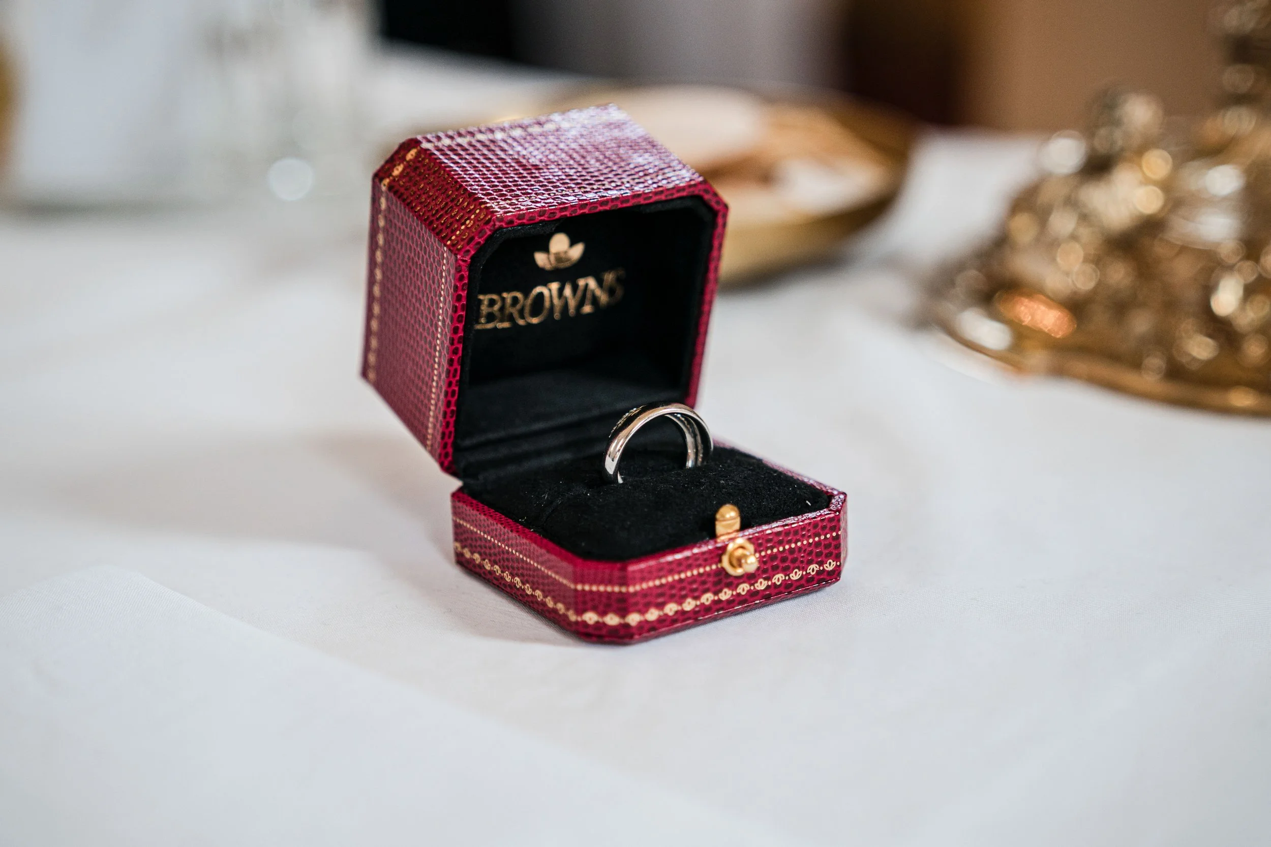 Ein offenes Schmuckkästchen mit einem silbernen Ring und einem Gold-Donut-Charme auf schwarzem Innenfutter, auf einem weißen Tischtuch.