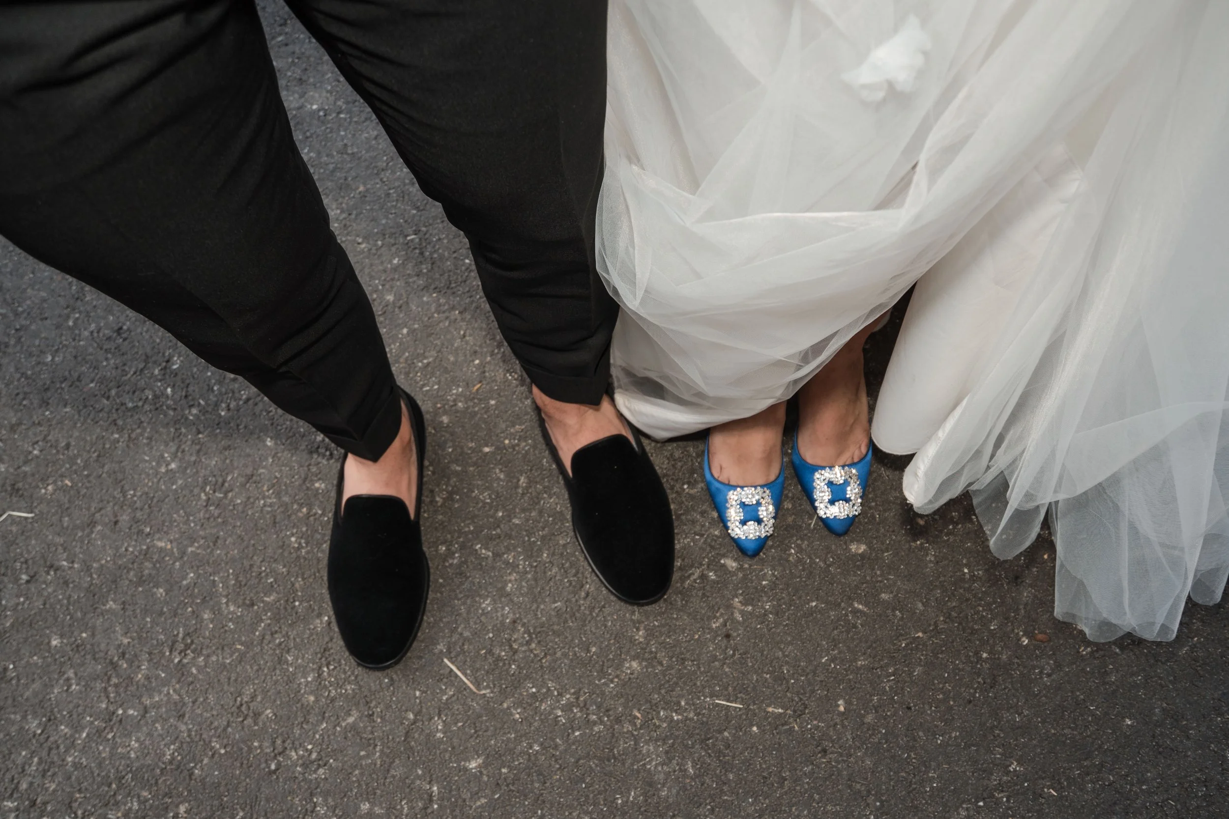 Paarfüße in formeller Kleidung und Hochzeitskleid auf einer asphaltbedeckten Oberfläche