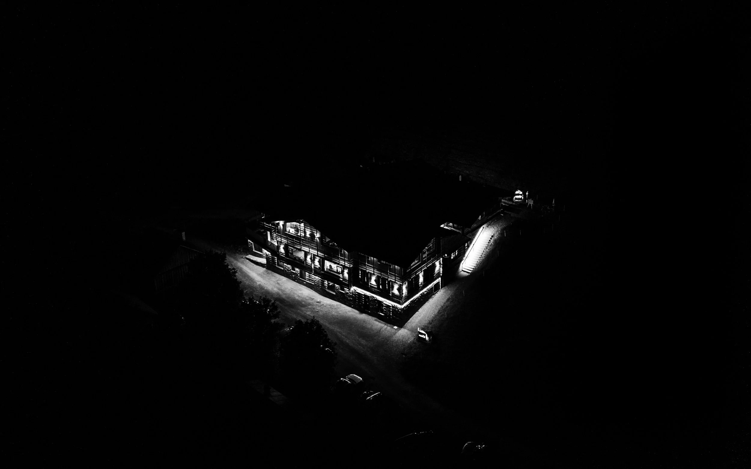 Eine beleuchtete, zweistöckige Holzhütte bei Nacht, umgeben von Dunkelheit, mit einem befestigten Weg vor dem Gebäude.