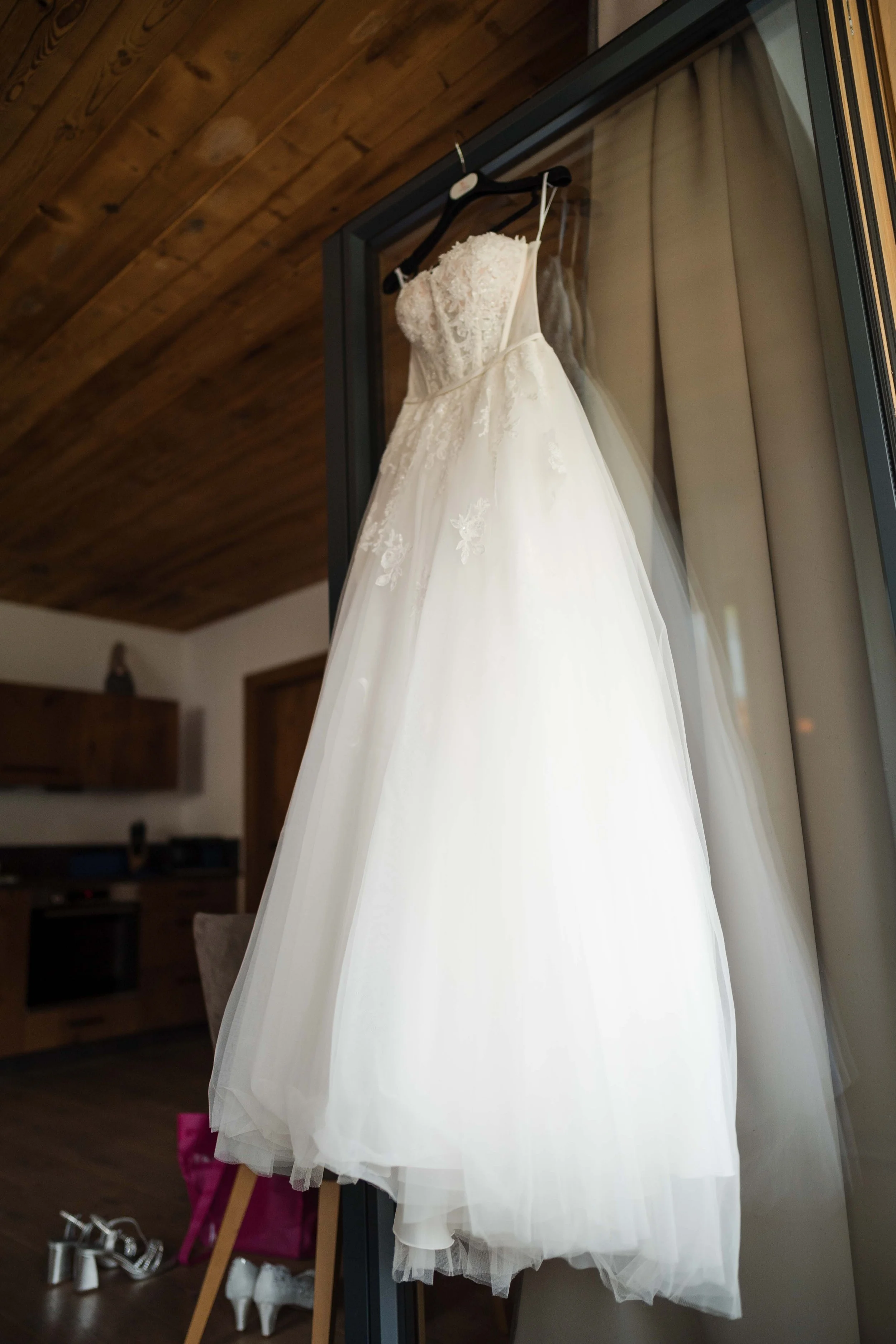 Weißes Brautkleid mit Spitzenapplikationen hängt an einem schwarzen Kleiderbügel vor einem Spiegel.