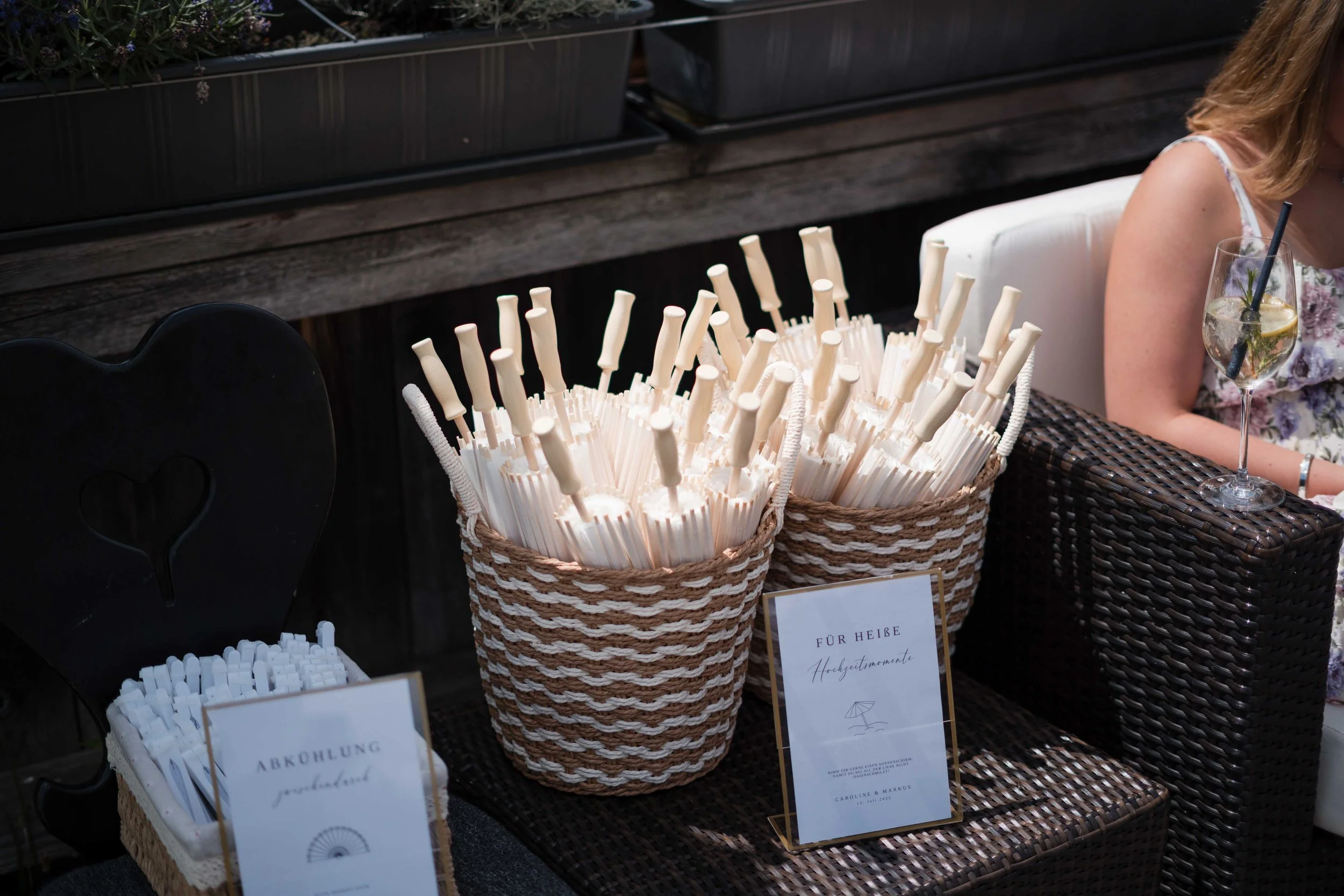 Zwei Körbe mit weißen Trinkhalmen mit weißen Griffen, eine Tafel mit der Aufschrift 'Für Heiße Heißgetränke', ein schwarzes Herz mit Loch und ein Glas mit Getränk samt Zitrone und Strohhalm auf einem Tisch, umgeben von einer weißen Sitzgelegenheit.