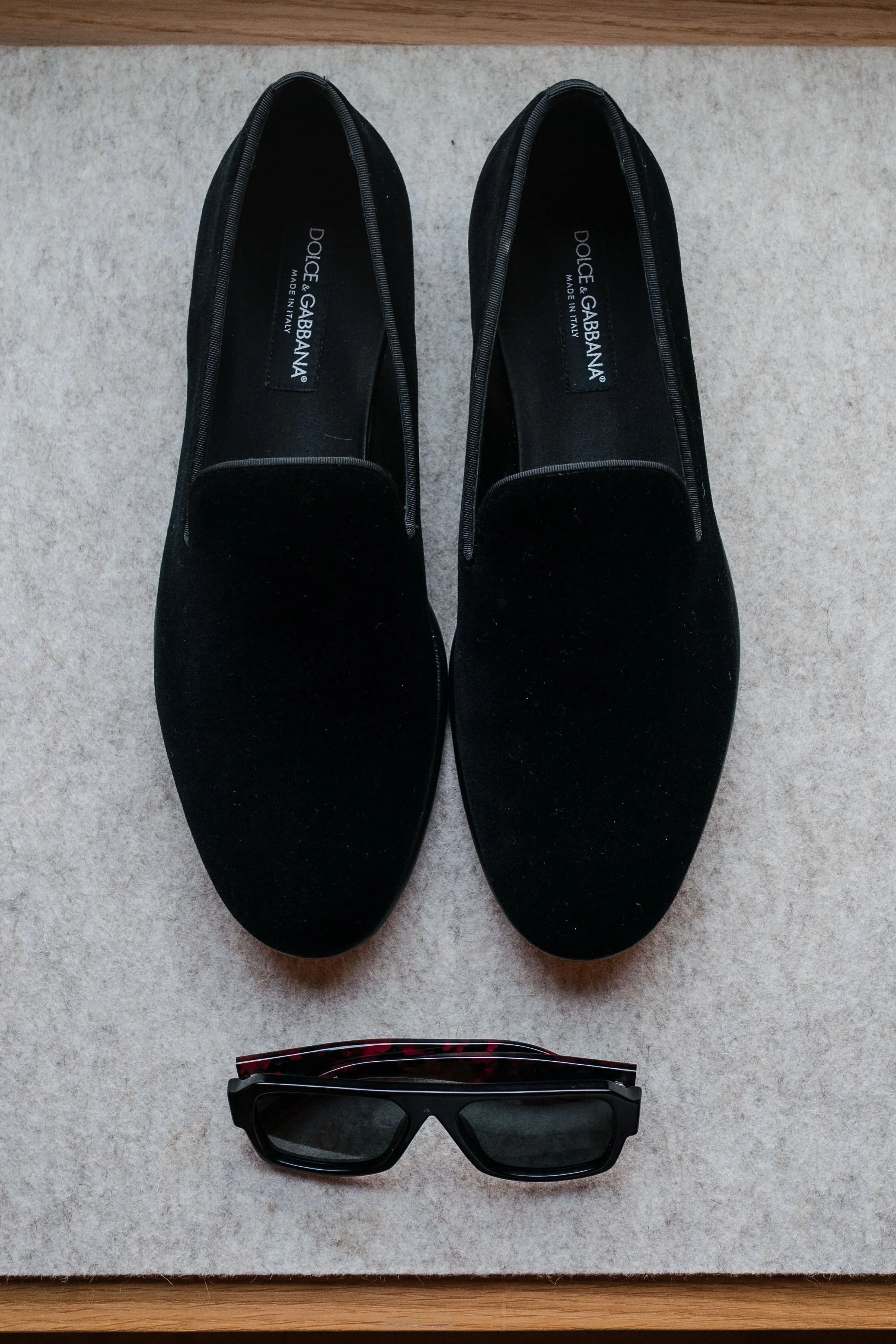 Ein Paar schwarze flache Schuhe und eine Sonnenbrille liegen auf einem Teppichboden.