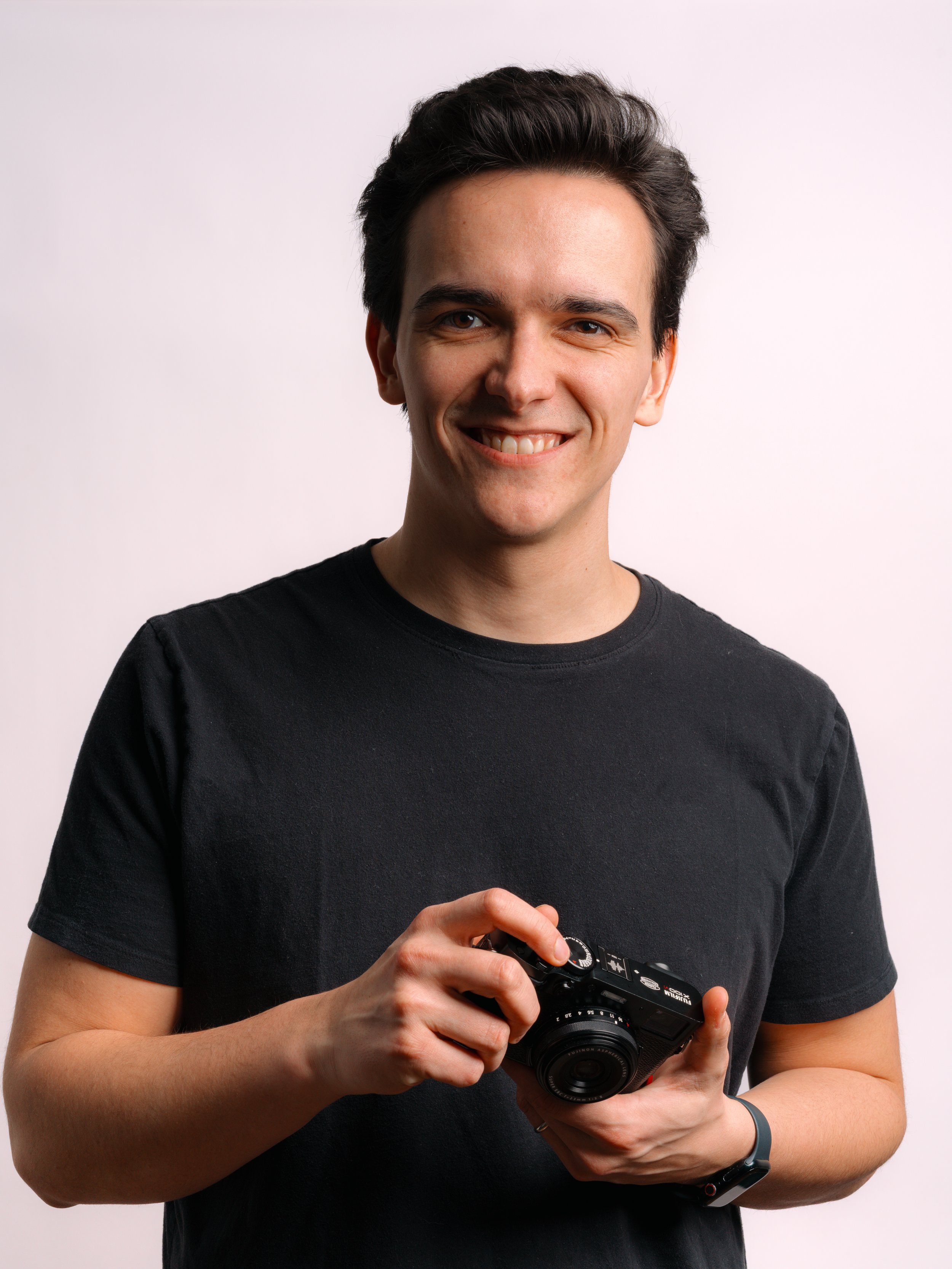 A smiling young man holding a camera in front of a plain white background. Studio headshot for business branding in Indianapolis Indiana