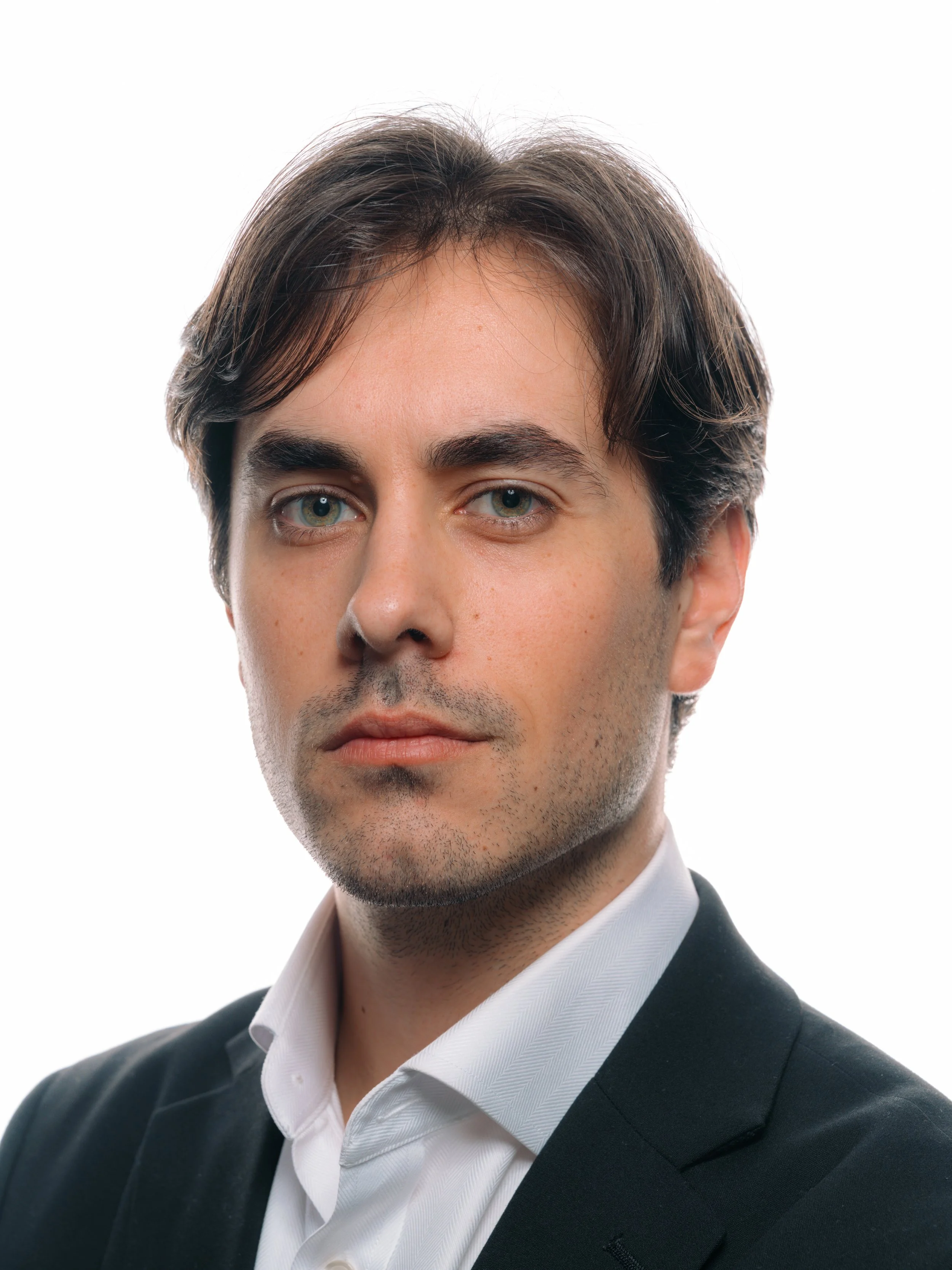 Professional headshot of a man with dark hair, blue eyes, wearing a white shirt and black blazer, against a white background. Professional headshot of business professional in Indianapolis studio lighting