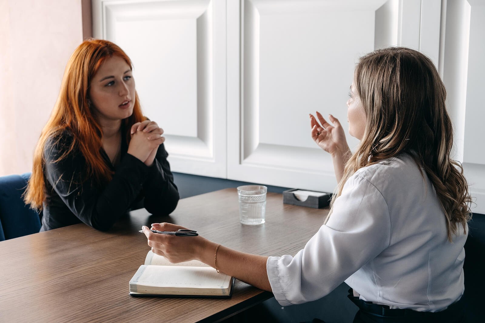 Two women sit across a table talking, one gesturing while the other listens, much like a session with a psychoanalytic therapist in Washington, DC. A Psychoanalyst Washington, DC brings this to psychoanalysis Washington DC sessions