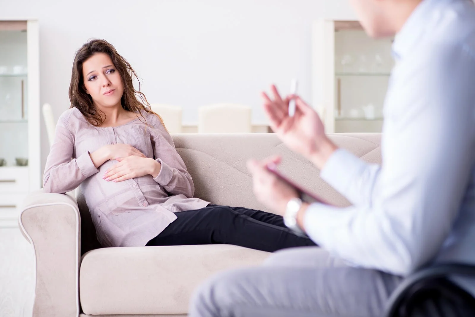 A pregnant woman sits on a couch sharing her worries with a postpartum anxiety therapist Washington DC, the kind of attentive care central to postpartum therapist Washington DC and postpartum anxiety therapy Washington DC.