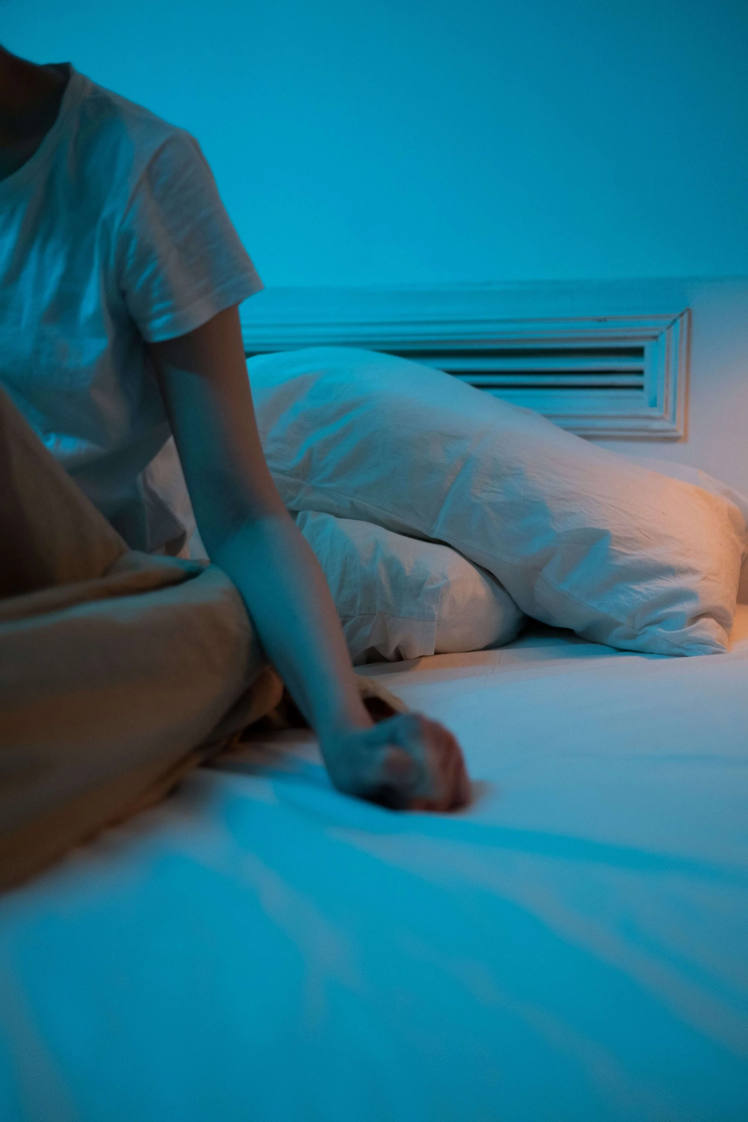 A restless figure reaches across the bed in blue night light, capturing sleeplessness tied to postpartum anxiety Washington DC, a sign of postpartum depression and anxiety Washington DC, often eased through postpartum anxiety therapy Washington DC.