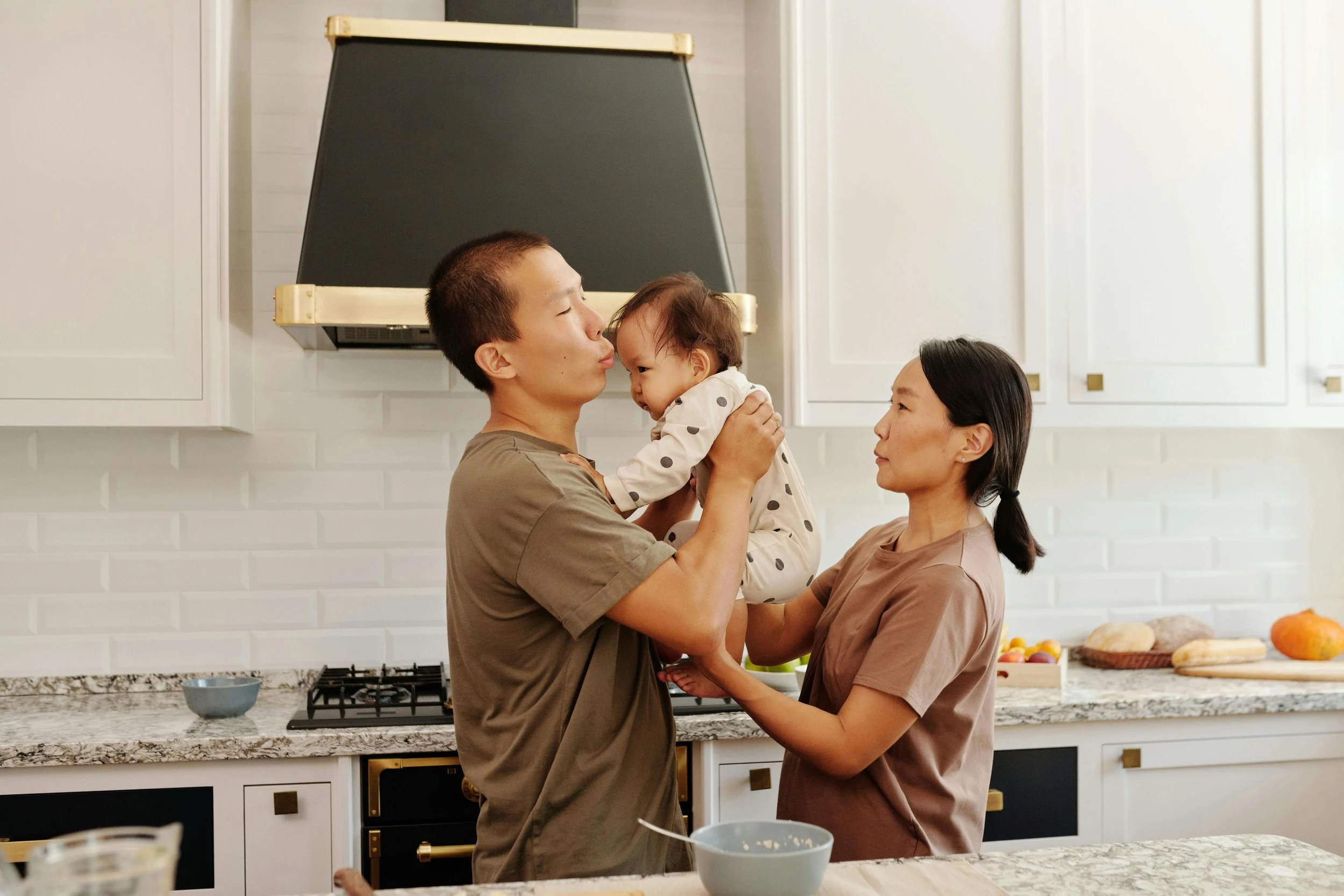 Mom and dad in the kitchen holding their baby while looking stressed, representing challenges addressed in postpartum therapy for cultural expectations in Washington, DC.