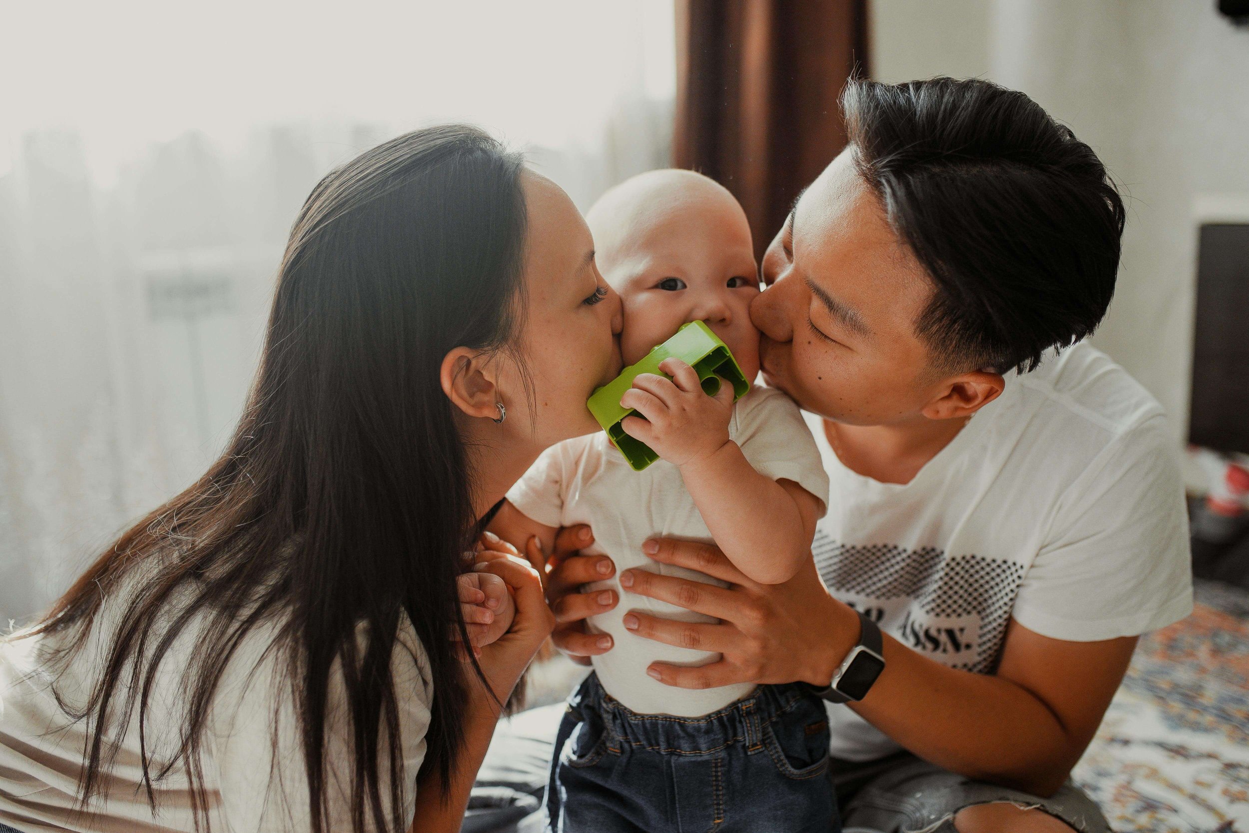 Mom and dad both kissing their baby at the same time, illustrating connection and support encouraged through postpartum therapy for new moms in Washington, DC.