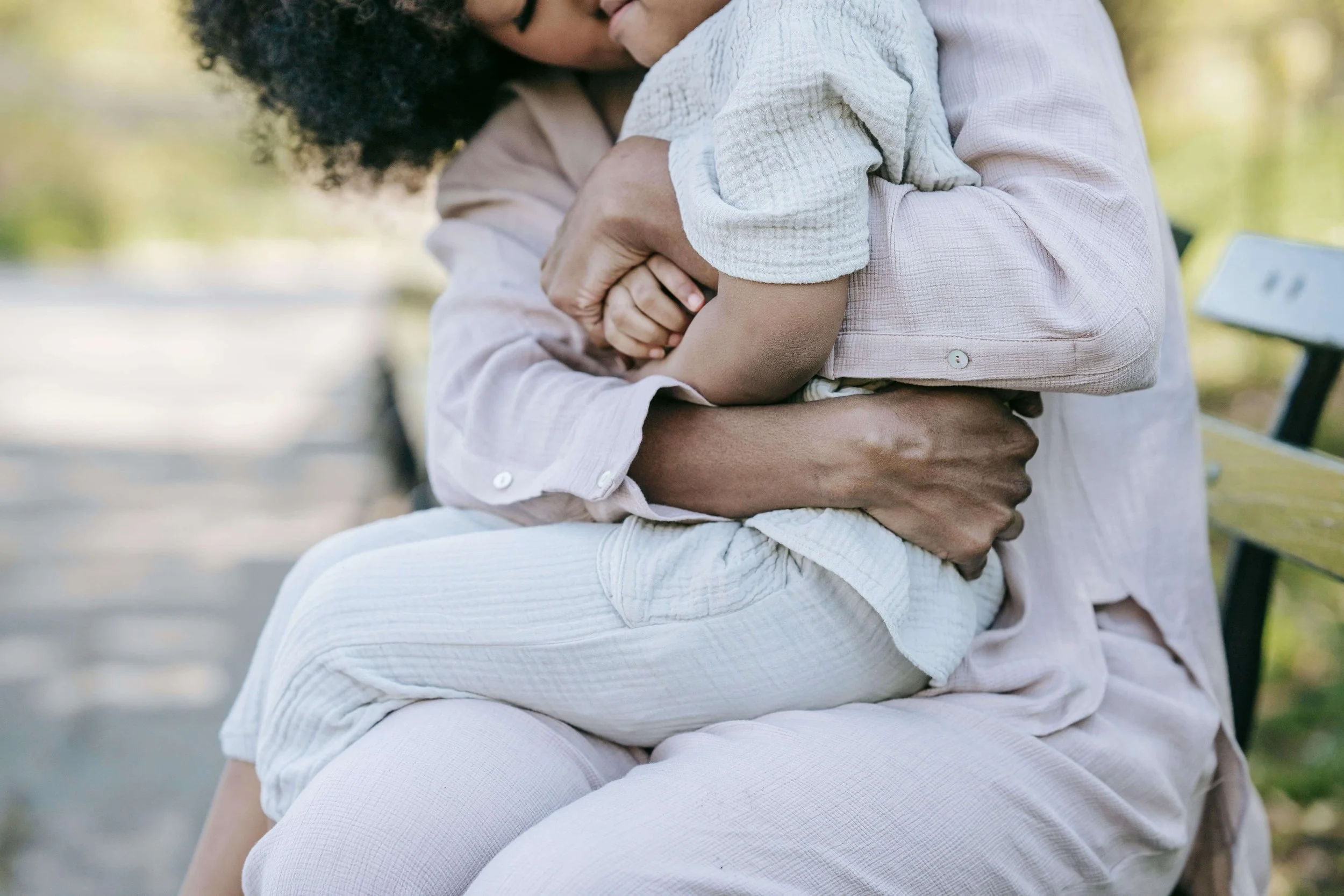 Parent sitting on a bench holding their baby securely, symbolizing connection, care, and healing during a postpartum identity crisis in Washington, DC.