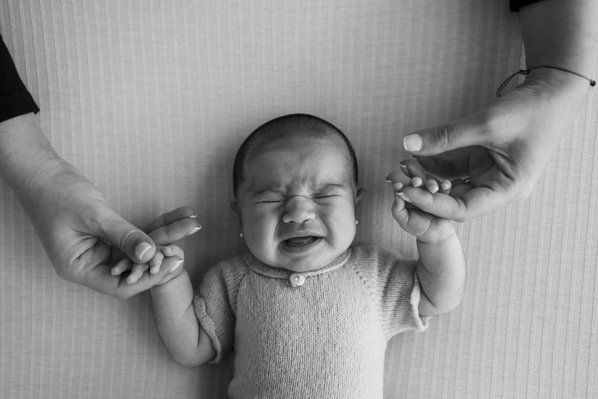 A black-and-white photo of a crying newborn gripping a mother's fingers. Love and overwhelm can coexist. Postpartum therapy for mom guilt in Washington DC and postpartum therapy for new moms in Washington DC ease the transition to motherhood.