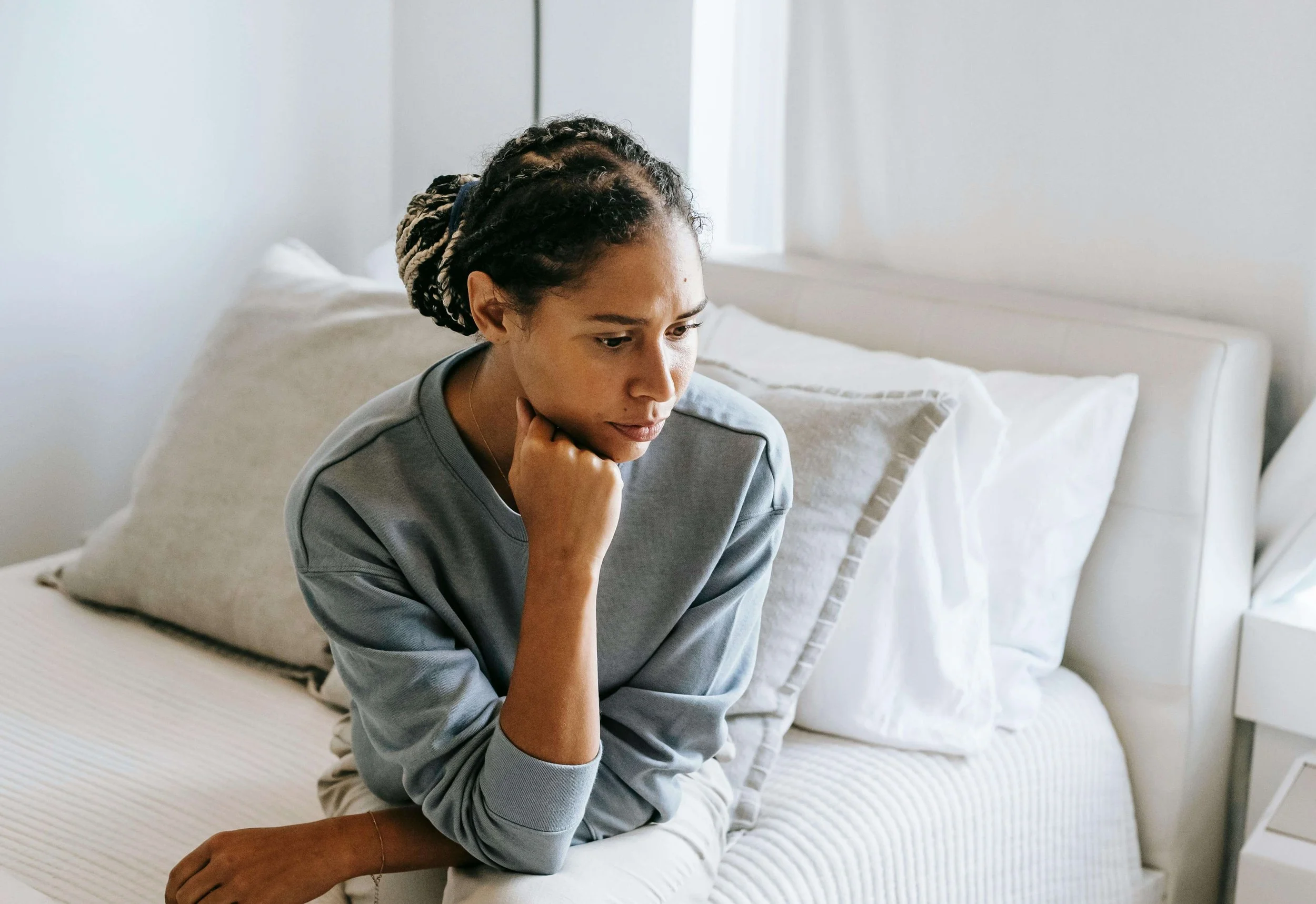 Woman sitting on the edge of a bed alone and thinking, illustrating emotional processing supported by psychodynamic postpartum therapy in Washington, DC.