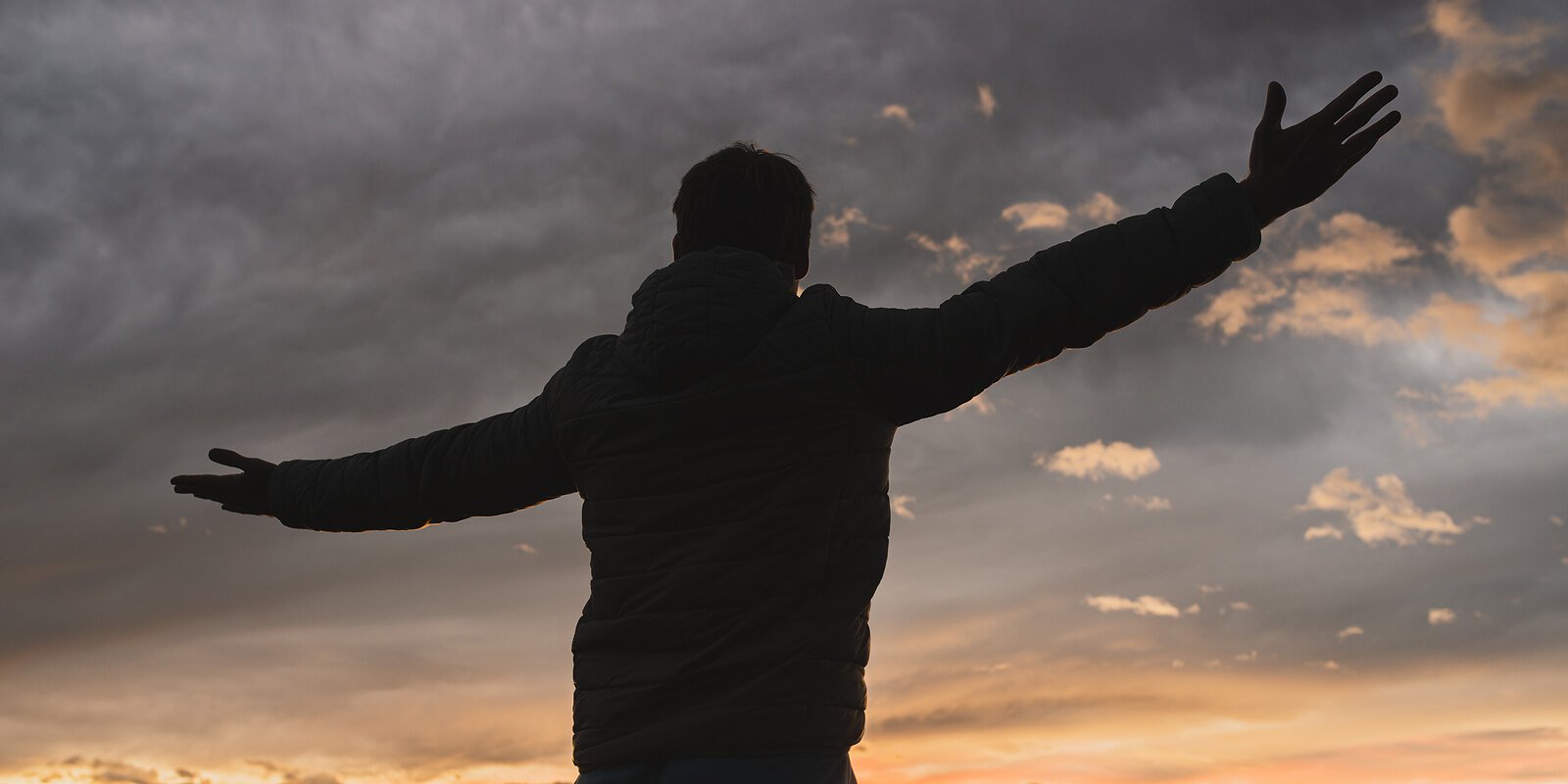 A man stands silhouetted against a sunset sky, arms outstretched, reflecting the freedom psychodynamic therapy in Washington, DC works toward. A psychodynamic therapist in Washington, DC using a psychodynamic approach in Washington, DC can help.