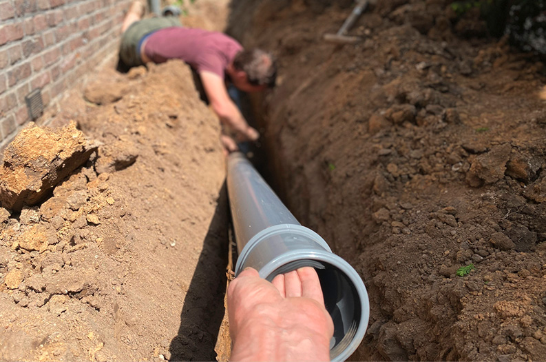 Person installing a large pipe in a dug trench.