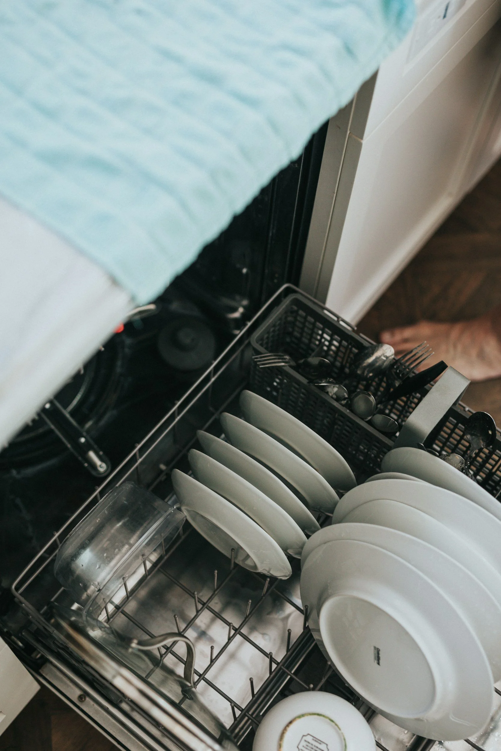 Open dishwasher full of plates, Tupperware, and lid to a pot.
