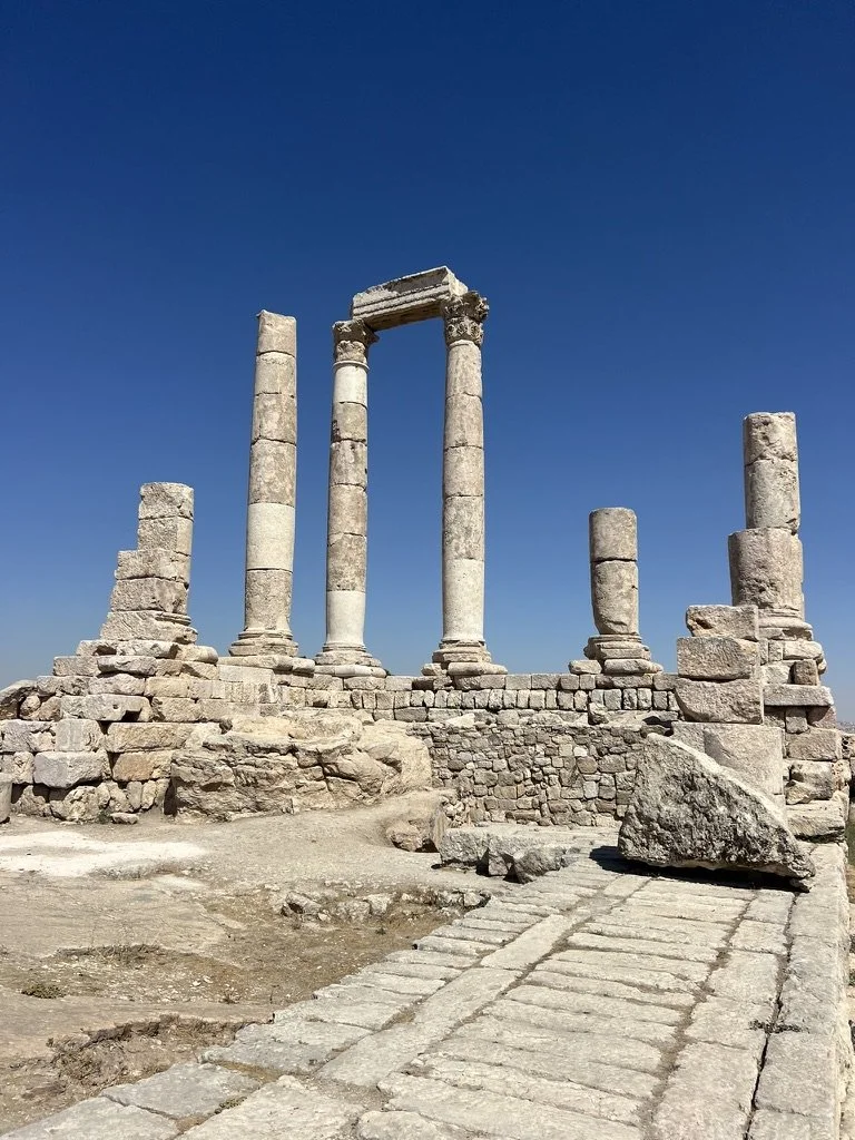 Ancient stone columns and ruins against a modern cityscape at sunset.