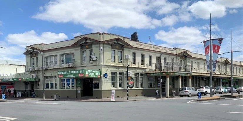 Historic building with a pub called Dargaville Sports Bar, located on a street corner with parked cars and a cloudy sky.
