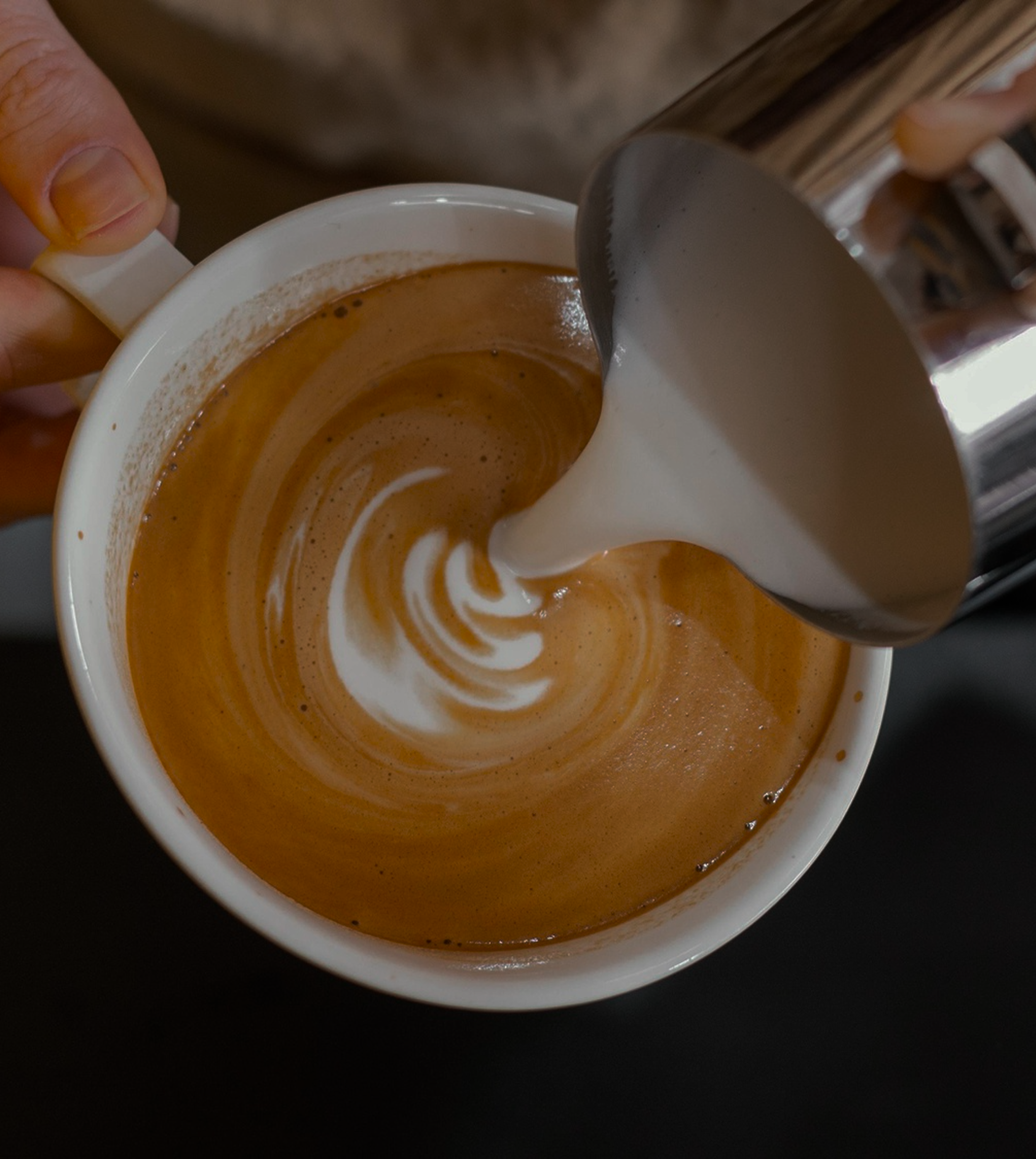 Coffee being brewed with milk pouring into it, creating a swirl pattern in a white cup.