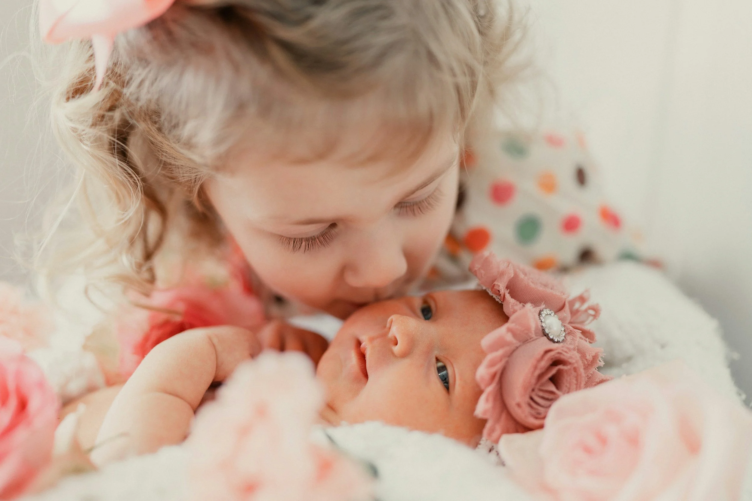 An older sibling gently kissing a newborn baby’s head, showing the transition to a growing family and sibling bond support at Early Bonds Therapy.