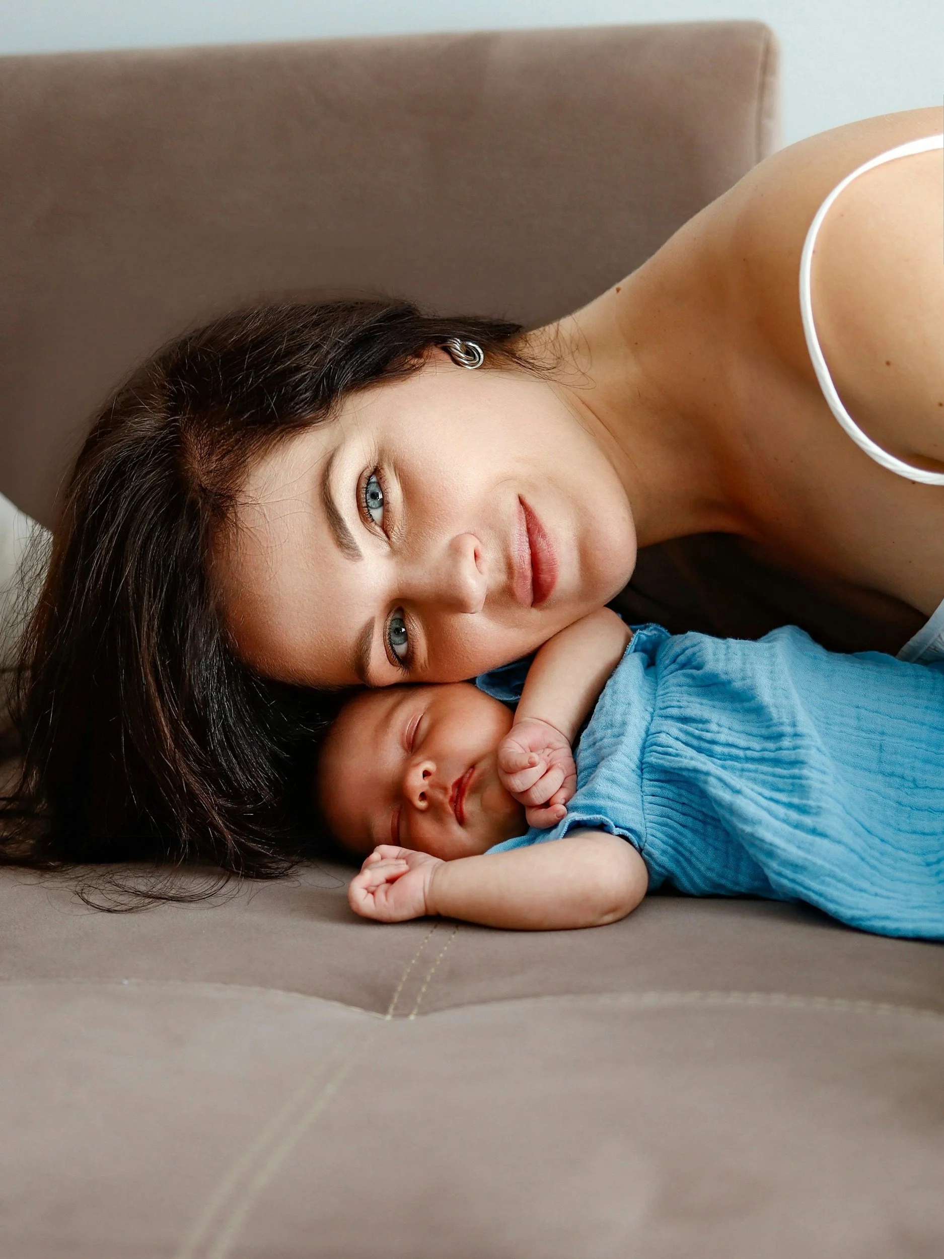 A mother resting her head on a sleeping newborn, representing the mental load and physical fatigue of the postpartum period.