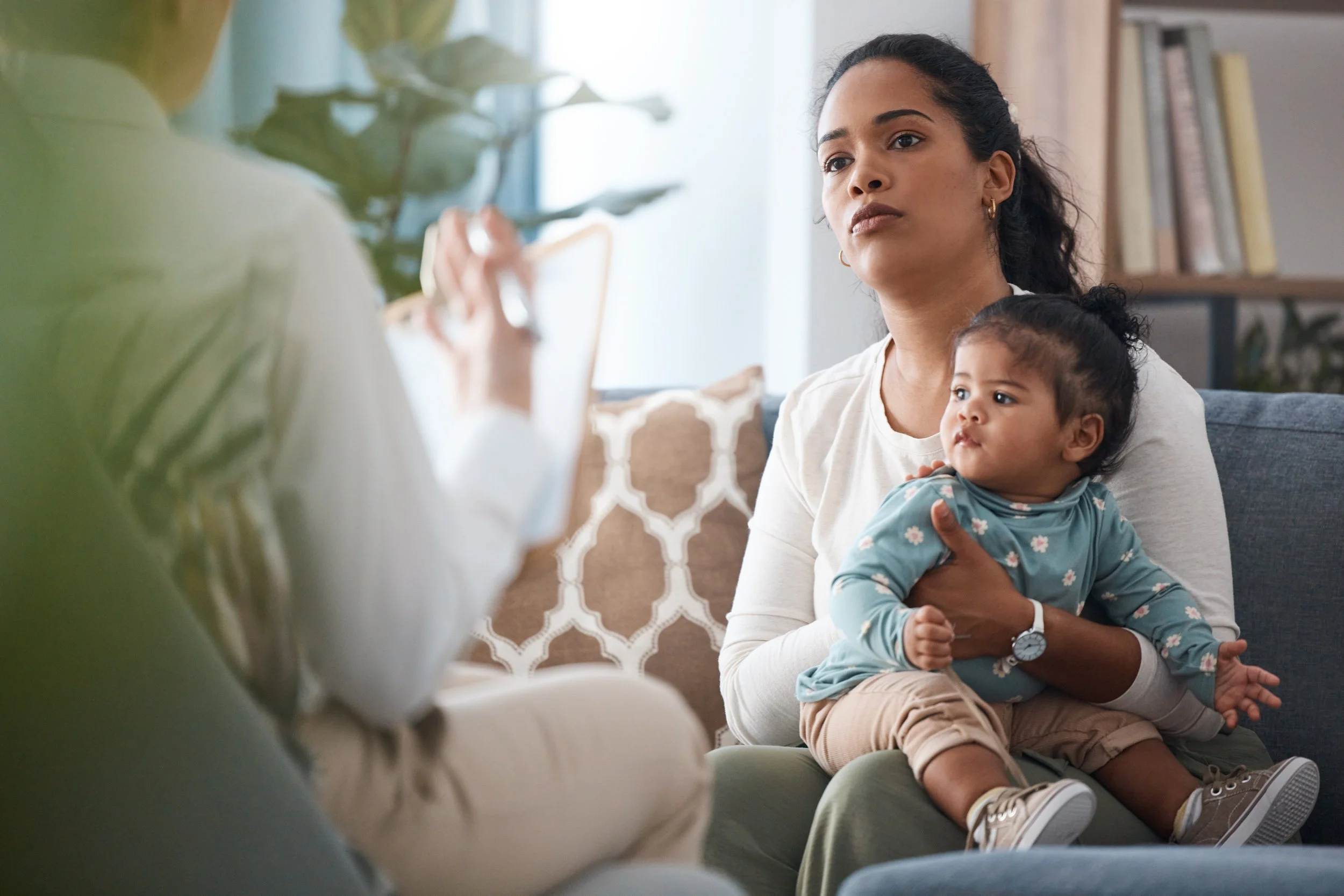 Mother holding a baby while listening to a therapist provide CBT strategies.
