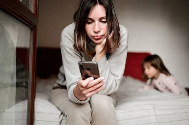 Mom sitting on bed looking at her phone scared and stressed by the newscycle