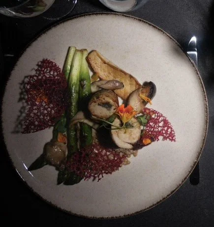 Assiette de cuisine gastronomique avec morceaux de viande, légumes et garnitures décoratives.