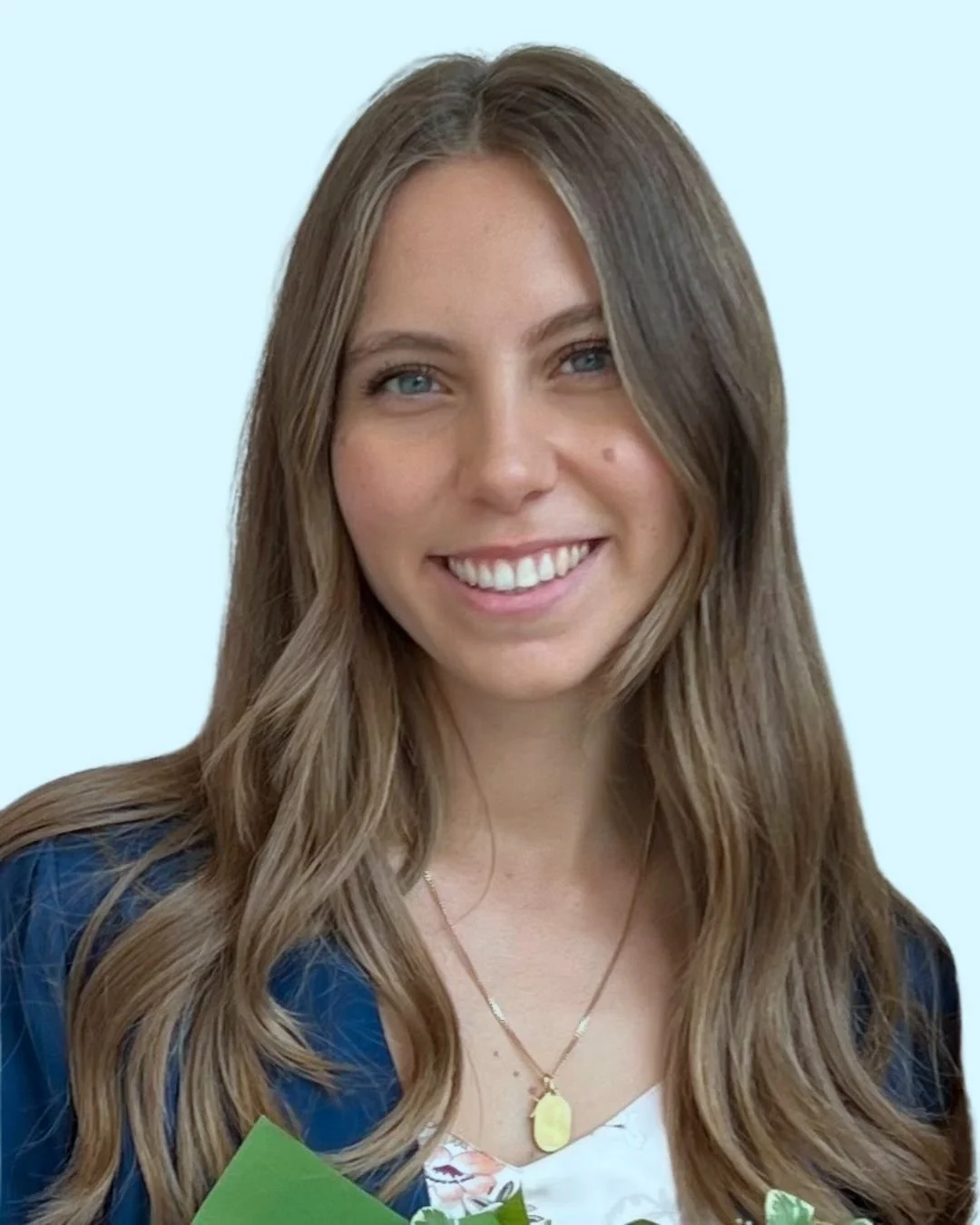 Una donna sorridente con capelli castani lunghi e occhi azzurri, indossa una collana d'oro e una giacca blu, sfondo azzurro chiaro.