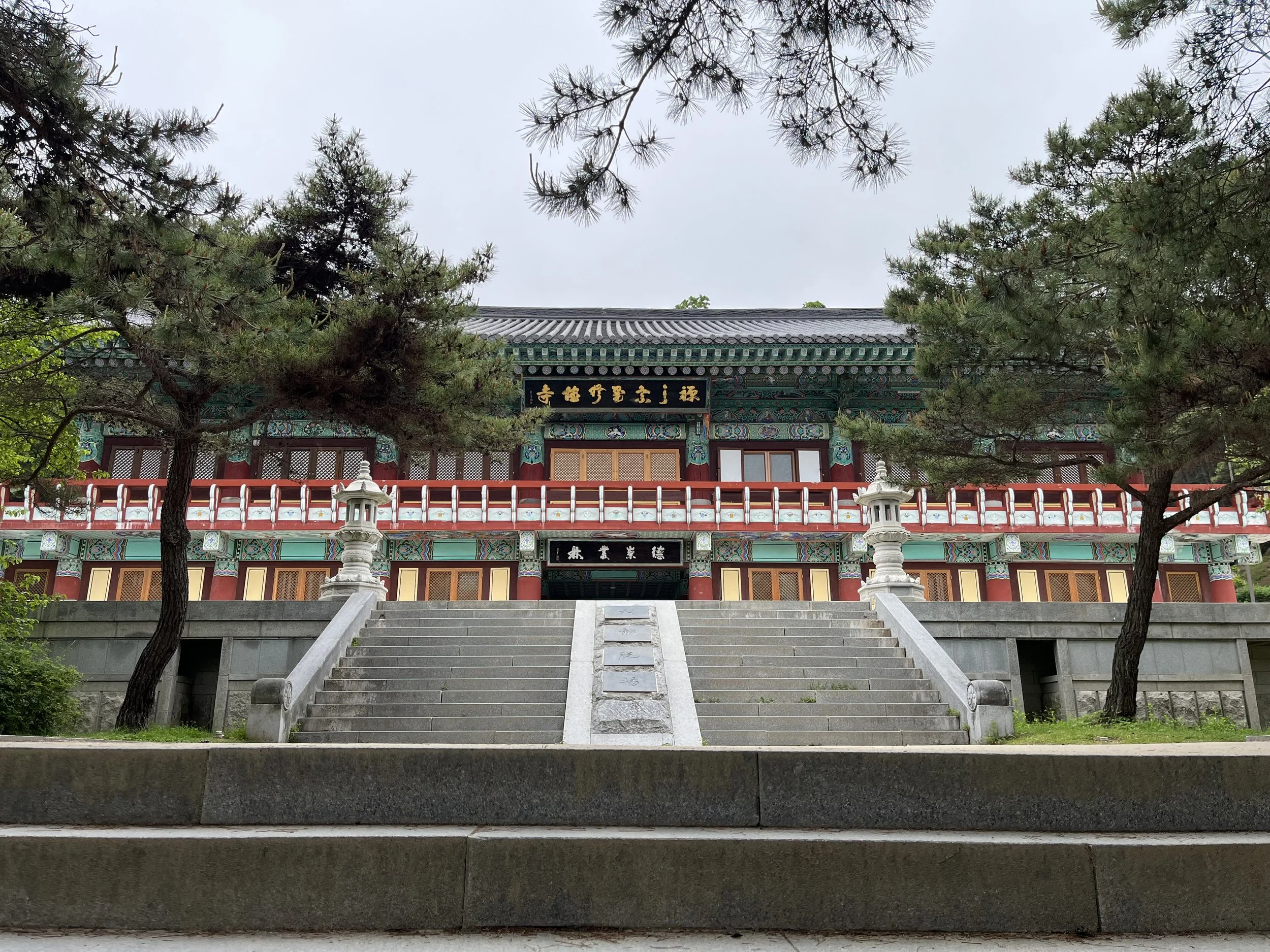 Traditional Korean temple building with stairs leading up to it, surrounded by trees.