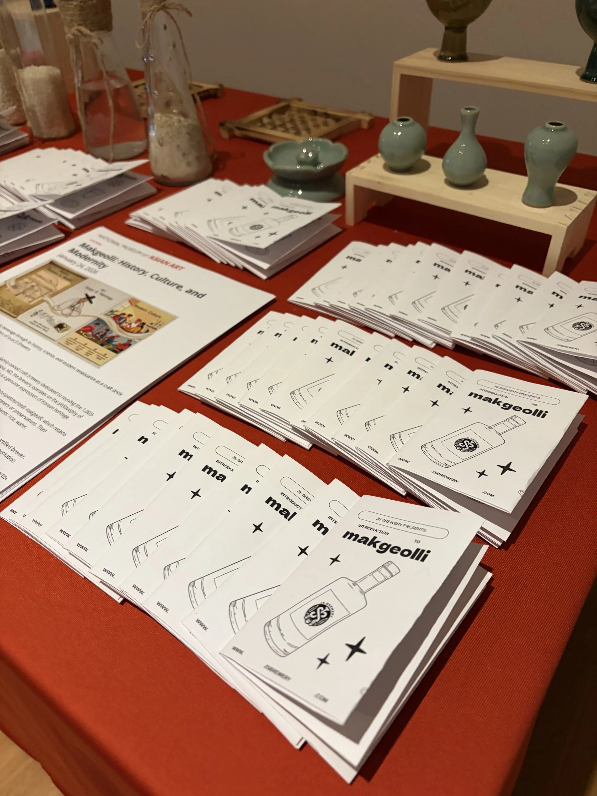 A bunch of colorful books sit on top of a wooden coffee table with black seats and a modern white seat behind.