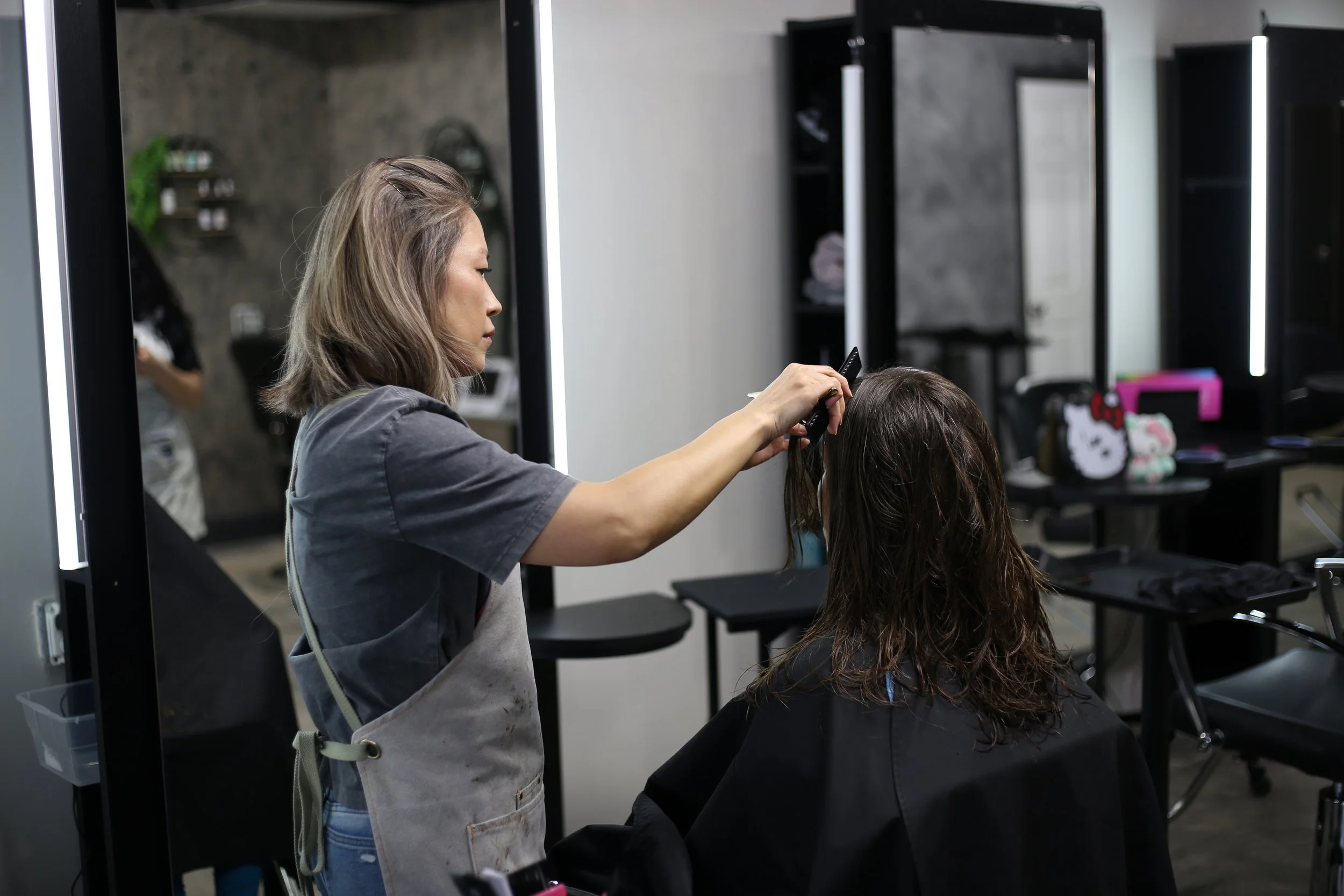 A hairstylist cutting a woman's hair in a salon with large mirrors and salon chairs