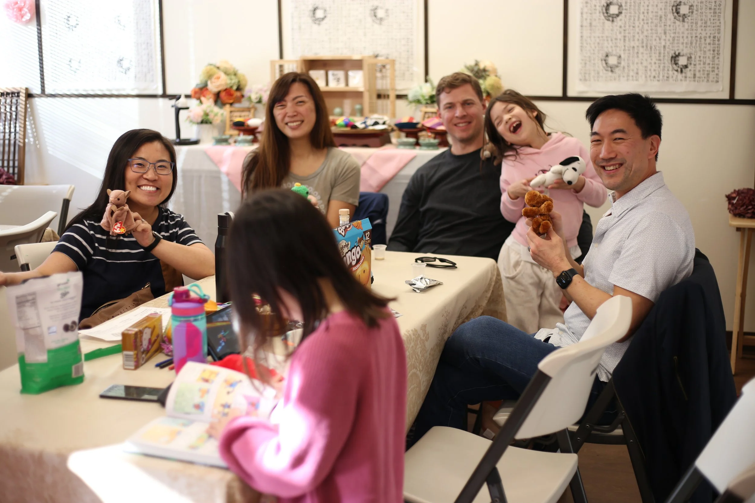 People sitting around a table smiling, with Valentine's Day gifts and toys, in a decorated room.