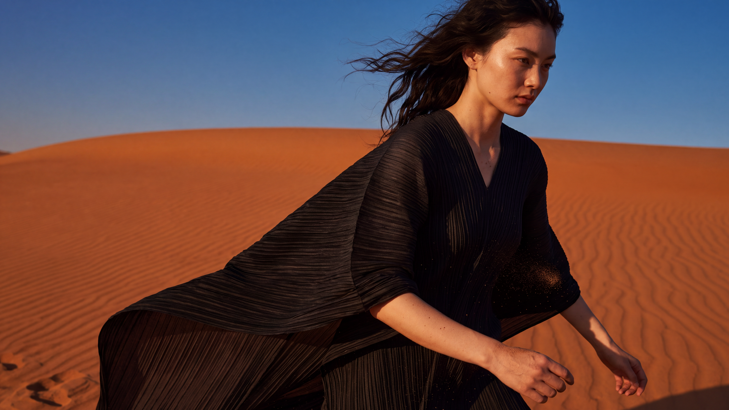 Maison Gia editorial featuring an Issey Miyake black dress photographed on sand dunes at sunset.