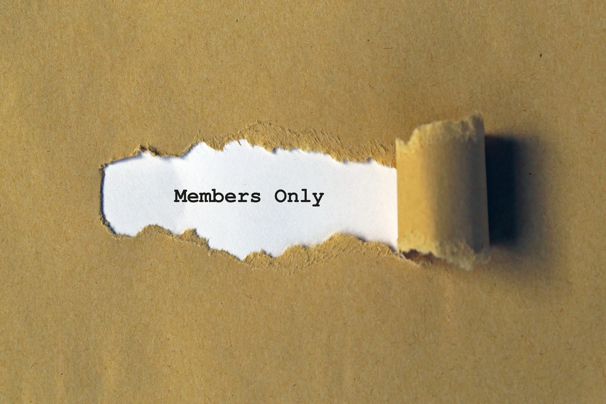 A sheet of brown paper with a torn opening, revealing a white piece of paper inside that has the text 'Members Only' typed on it.
