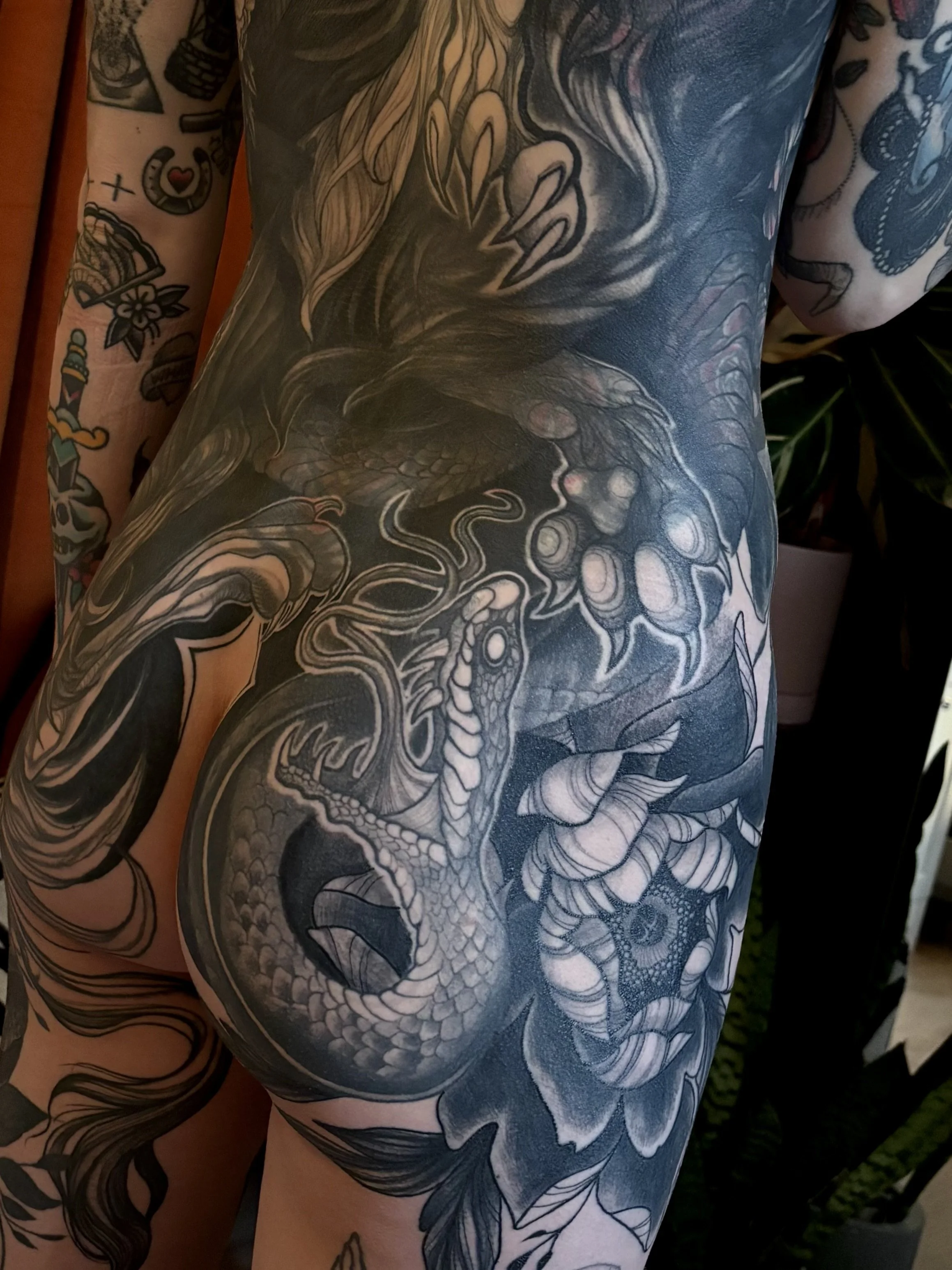 Black and gray full back piece tattoo of a snake coiled around a flower on a person's buttock.