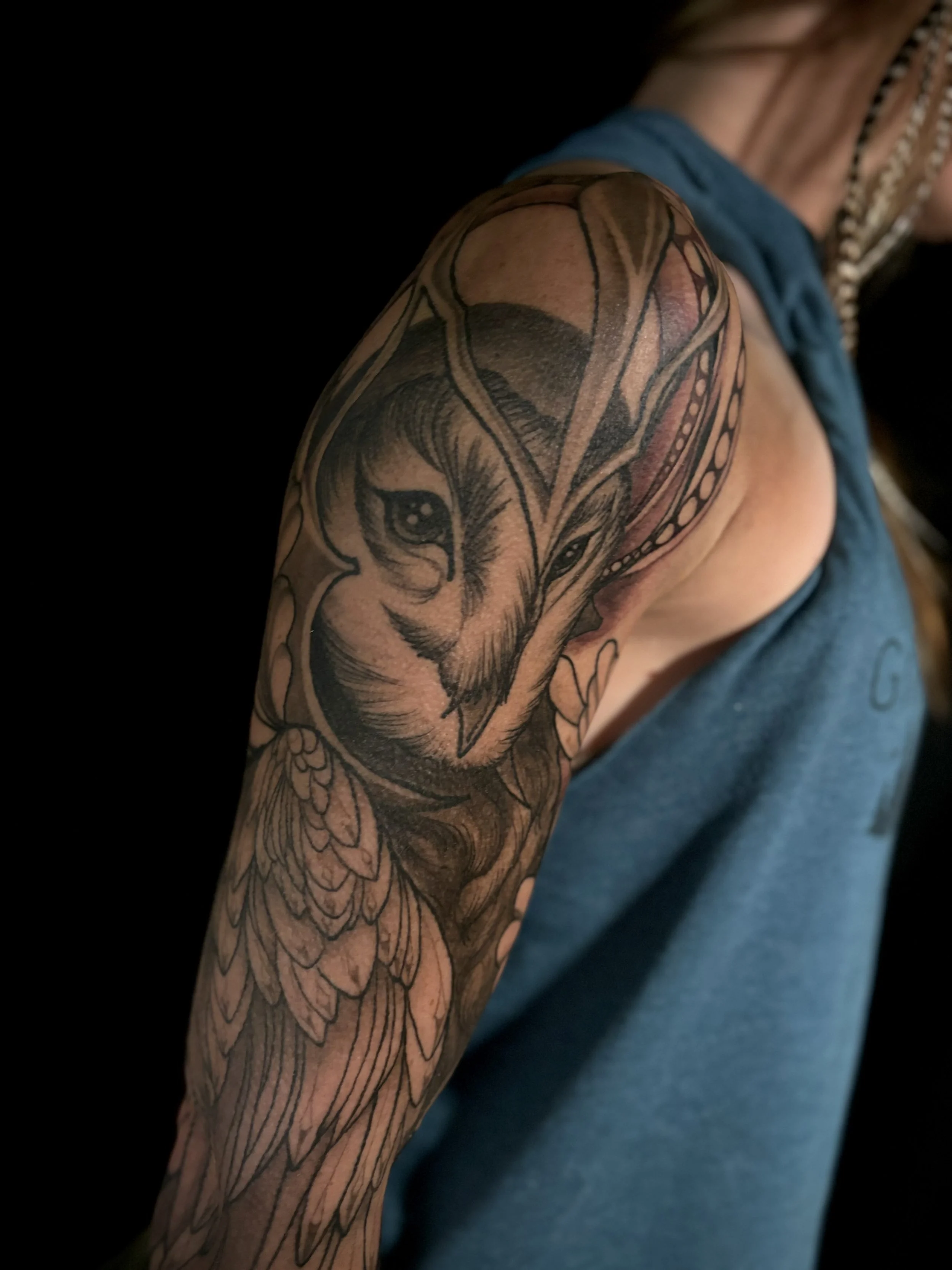 Close-up of a detailed black and gray tattoo of a barn owl wearing a battle helmet, symbolizing the goddess Athena on a person's upper arm.