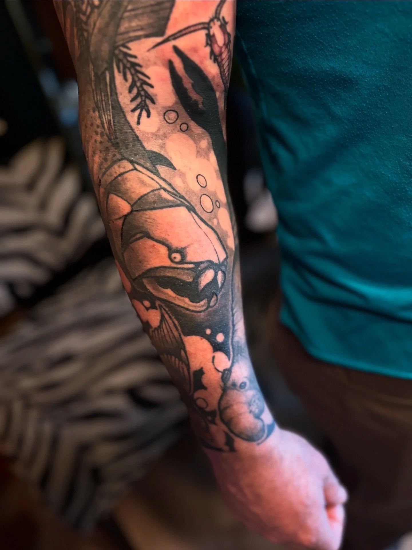 Tattoo of a prehistoric plated fish called a Dunkleosteus with waves and bubbles on a person's arm.