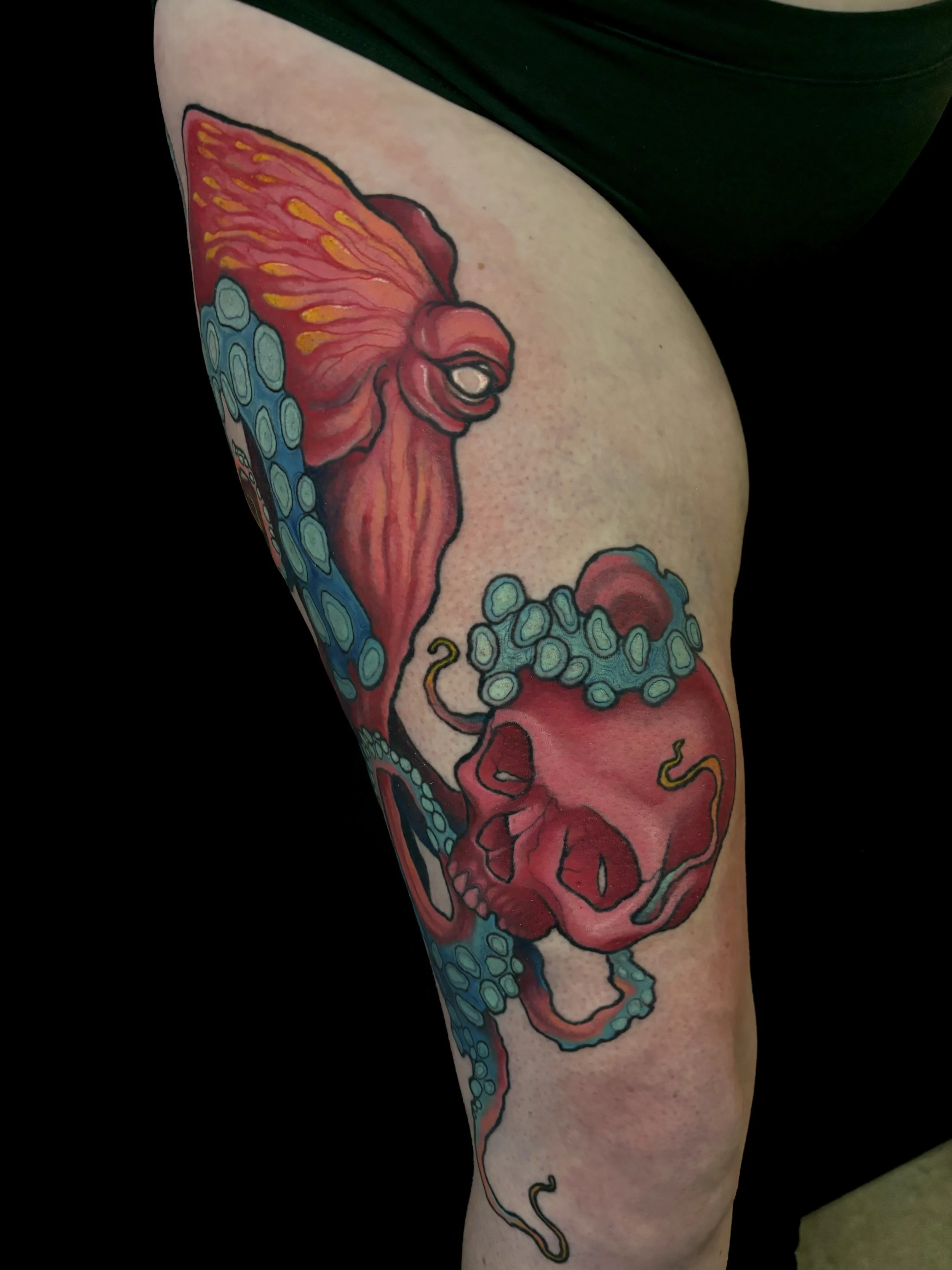 Colorful tattoo of a pink octopus with blue tentacles and a pink skull on a person's thigh.