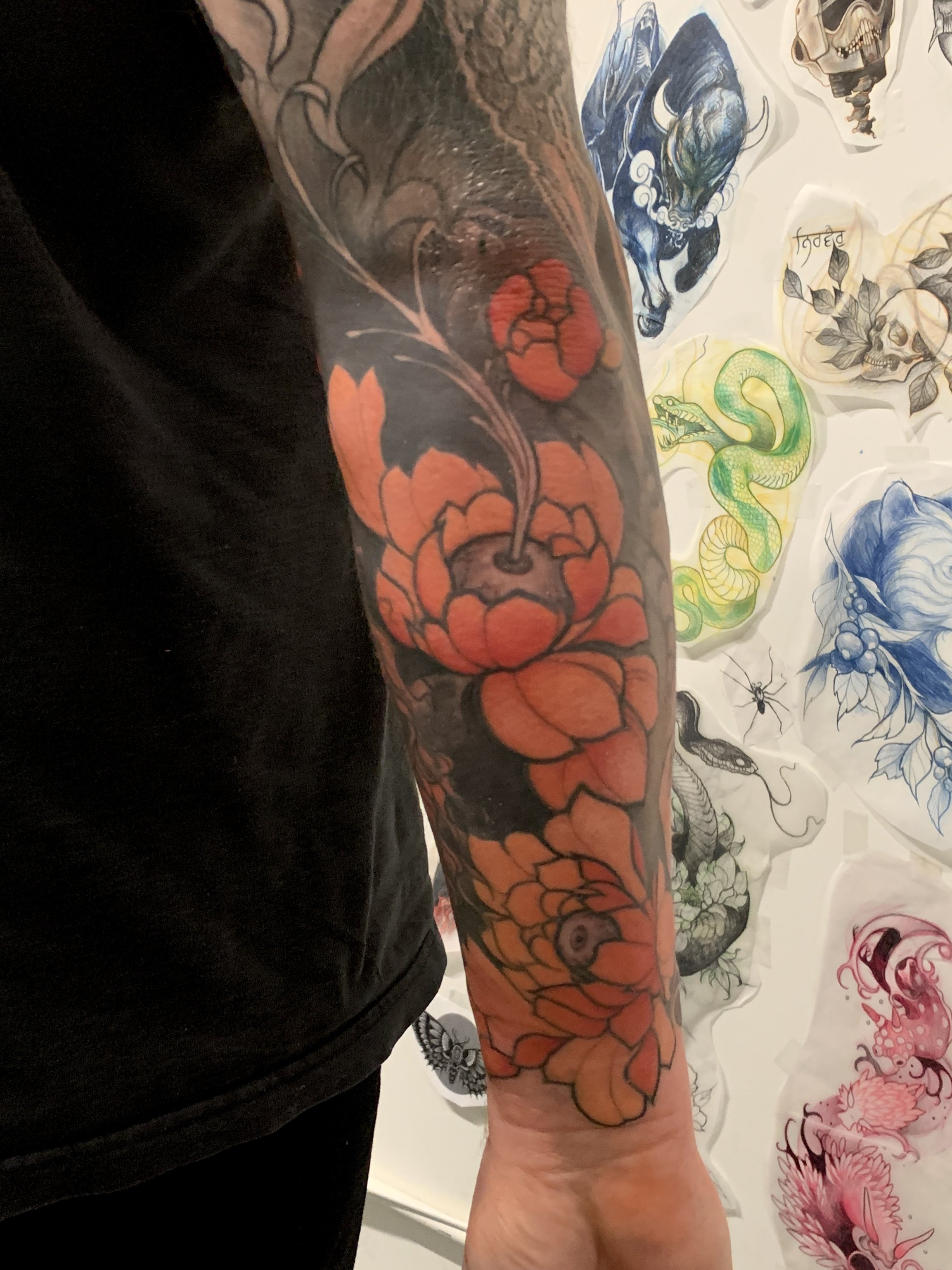 Tattoo of orange flowers with a snake on a person's arm.