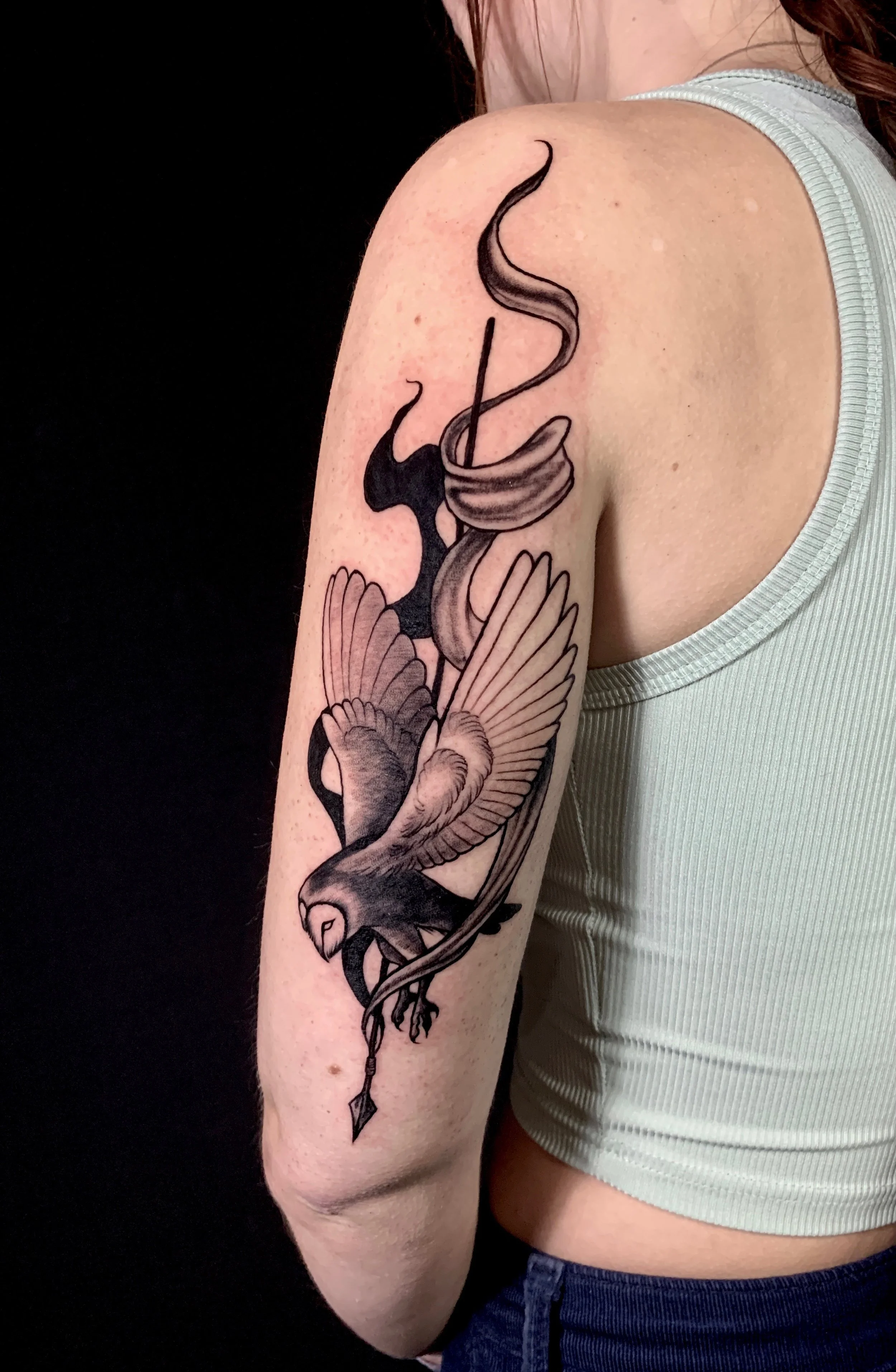 Black and grey tattoo of a barn owl, swooping down with a spear, symbolizing the goddess Athena.