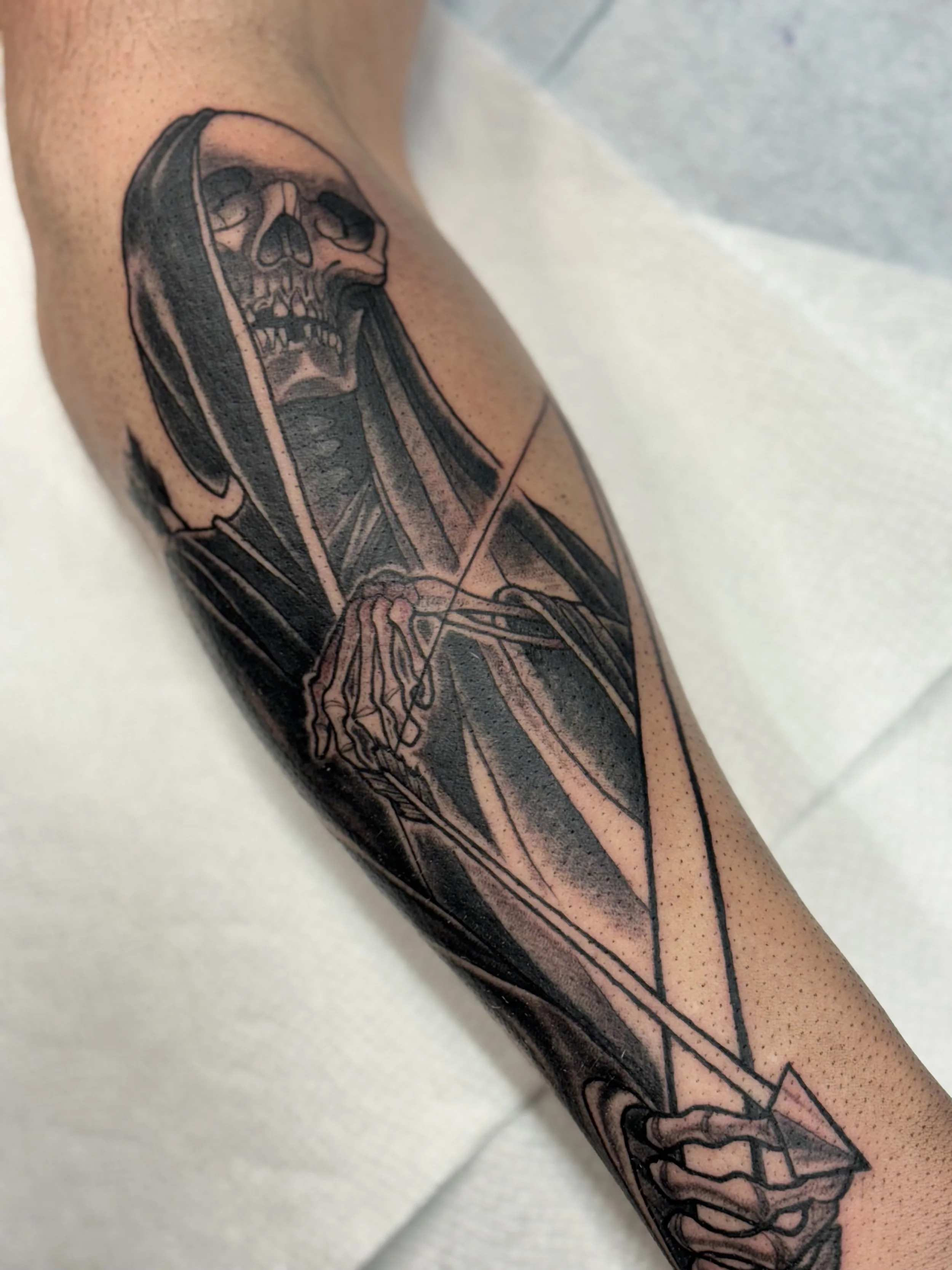 Black and gray tattoo of a skeletal hooded reaper ('death'), holding a bow and arrow.
