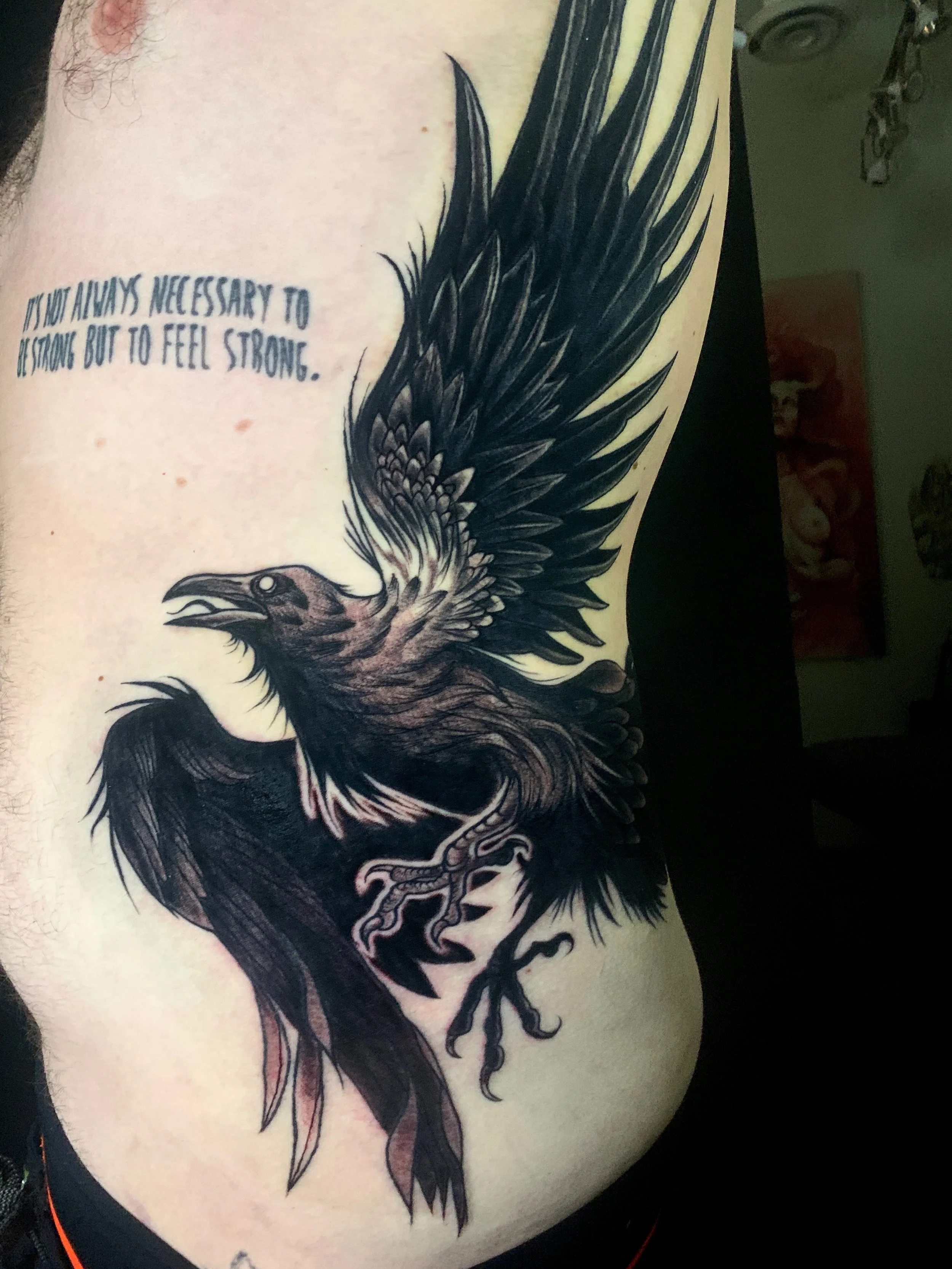 Black and gray tattoo of a soaring eagle on person's chest with the quote, 'It is not always necessary to be strong but to feel strong.'