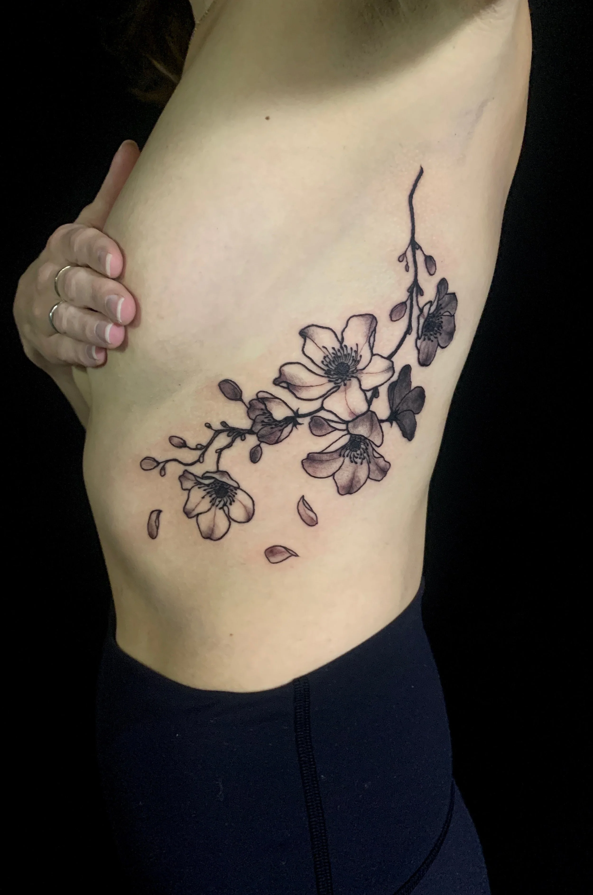 A floral tattoo featuring black and grey cherry blossoms on a woman's ribs.