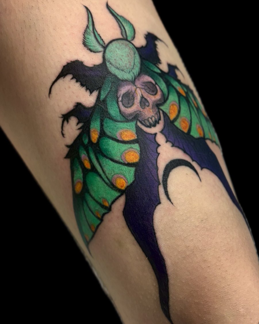 Colorful tattoo featuring a colourful moth with green wings and a skull appearing on its back.