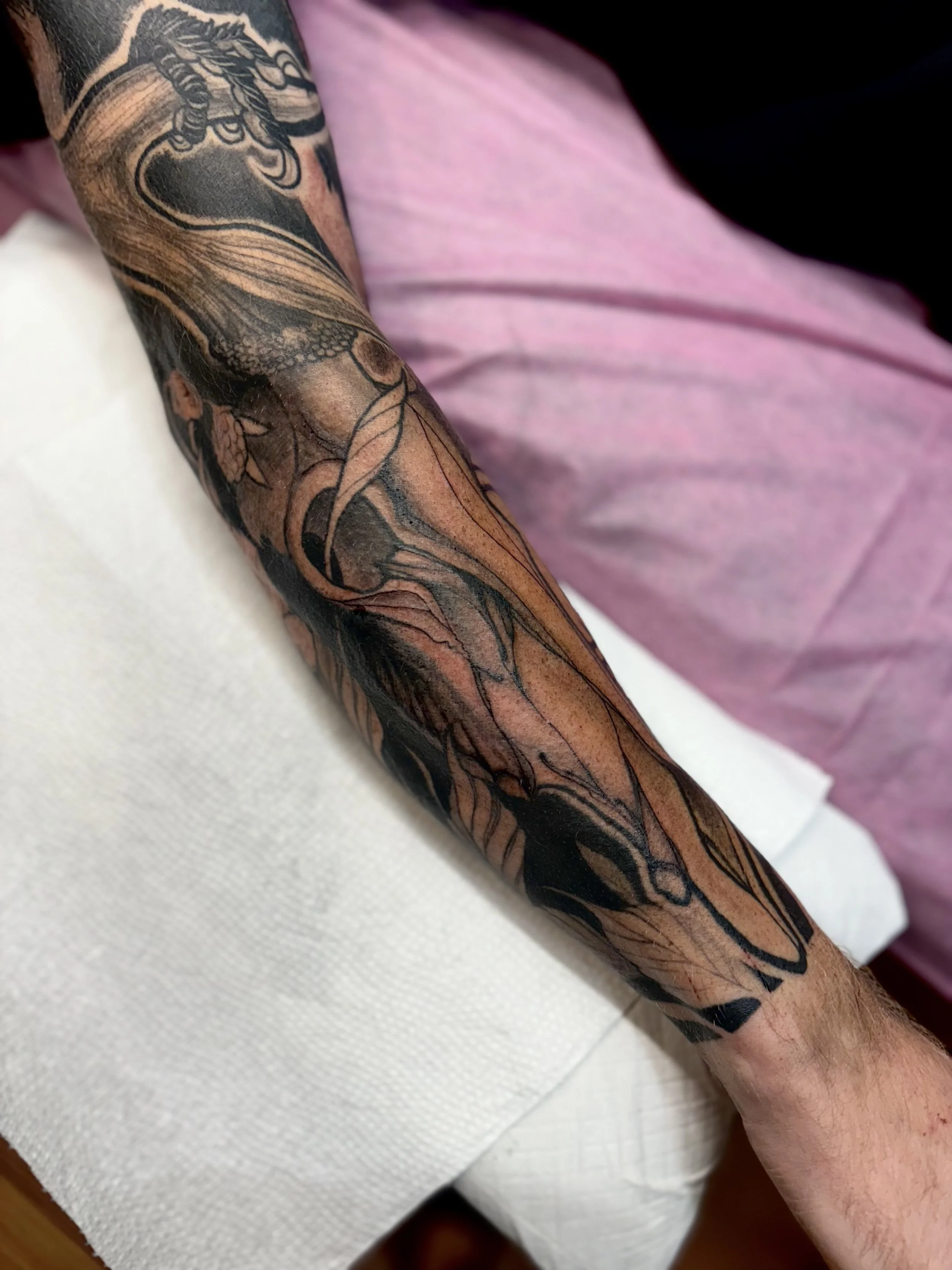 A tattoo sleeve on a person's arm featuring intricate black and gray line art with shading, depicting abstract and stylized artistic designs.