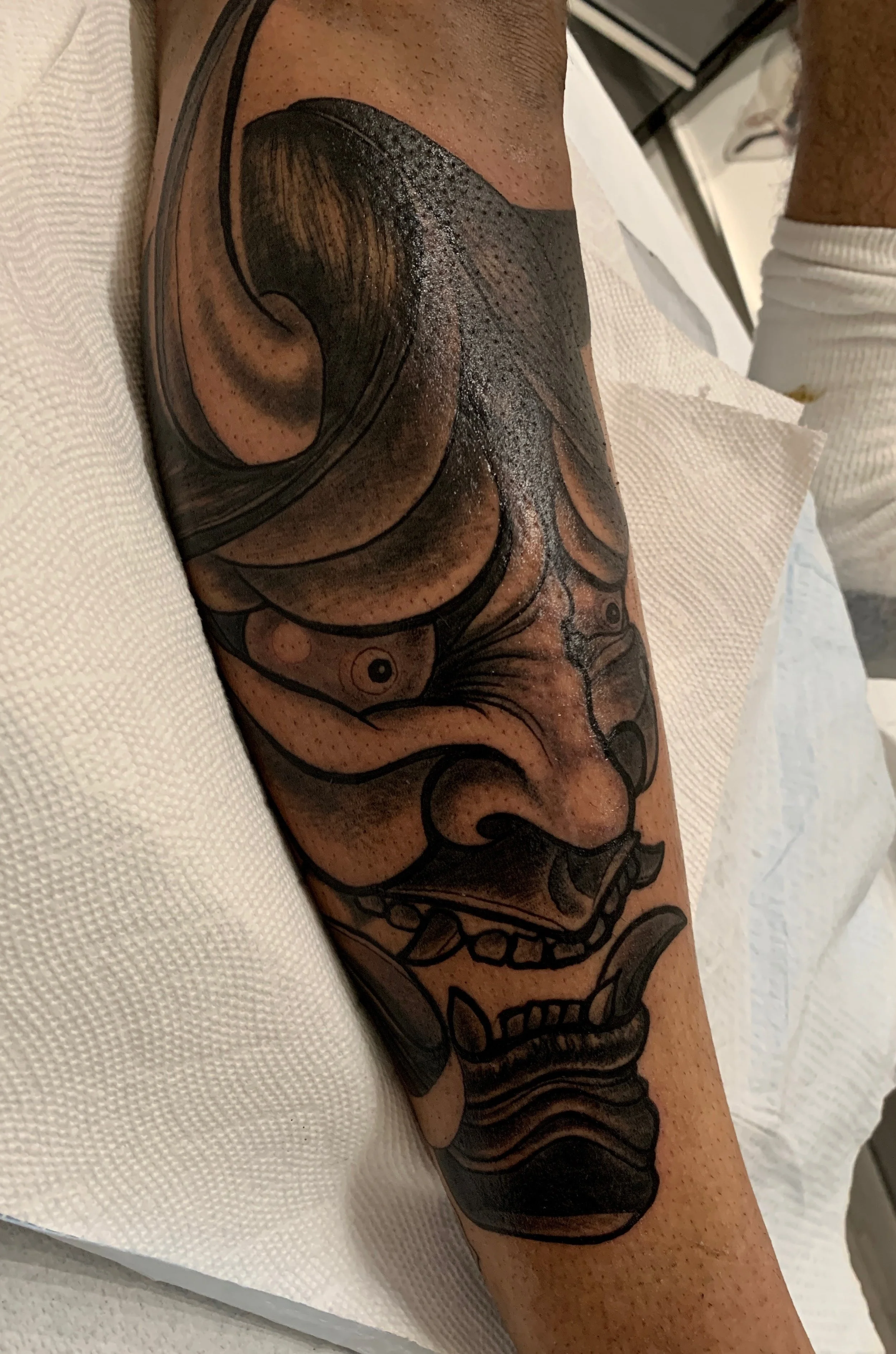 Close-up of a detailed black and gray tattoo of a hannya mask on a person's calf.