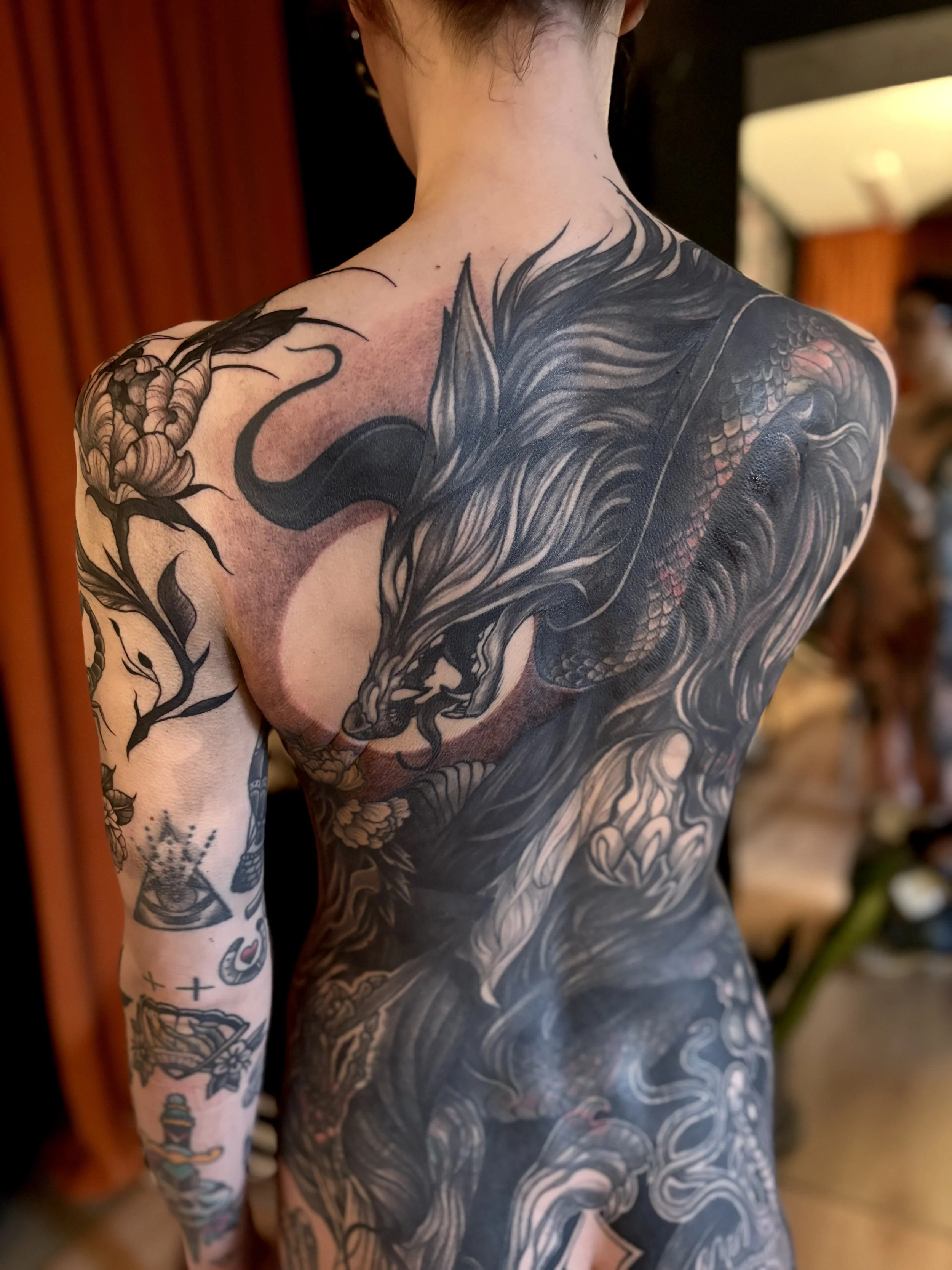 Back tattoo of a fierce wolf fighting a large snake surrounded by floral elements.