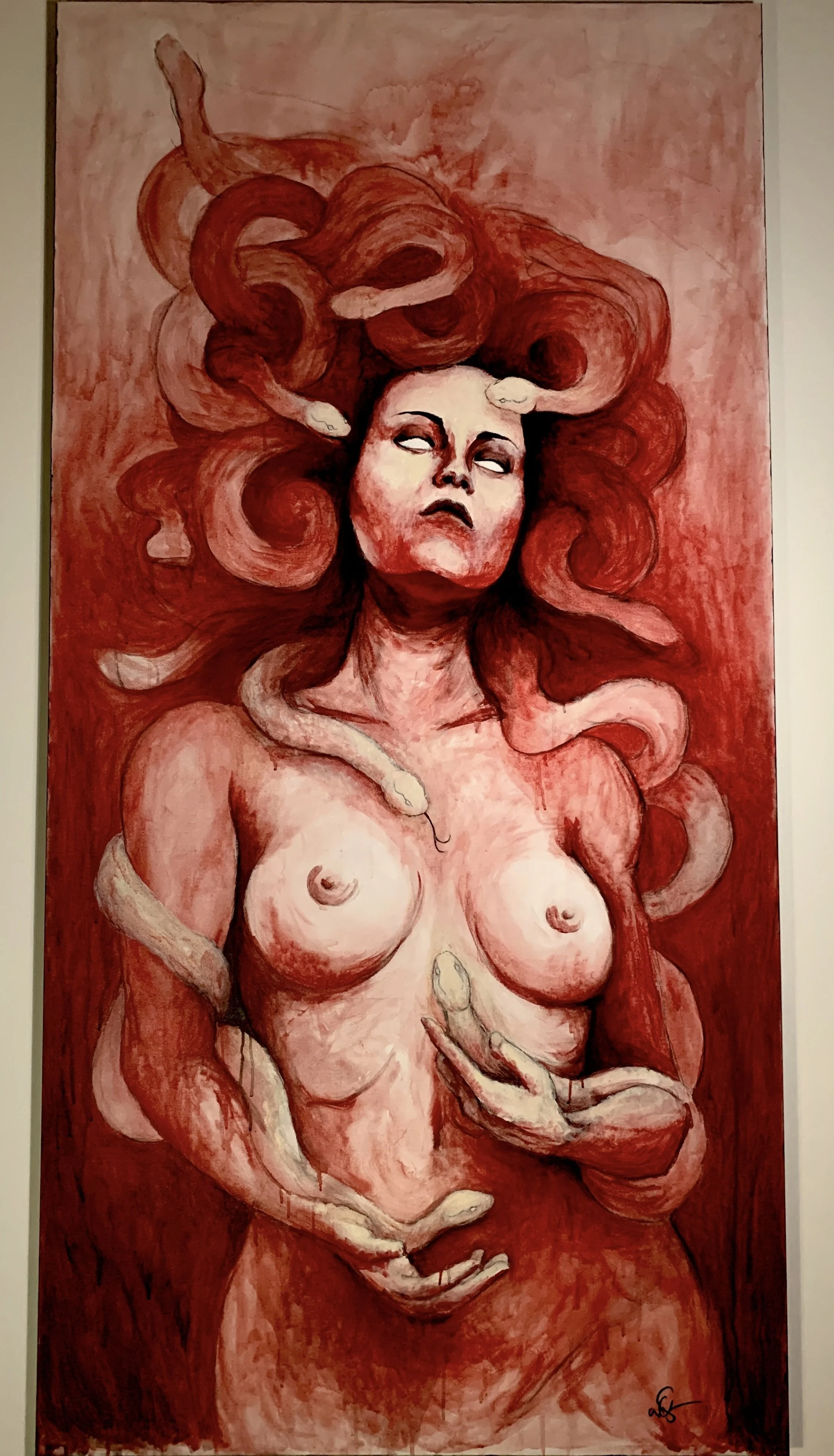 A painting of a topless Medusa with long, flowing hair that is made of snakes. Her eyes are blank, and her facial expression is serious. The color palette includes shades of red and black.