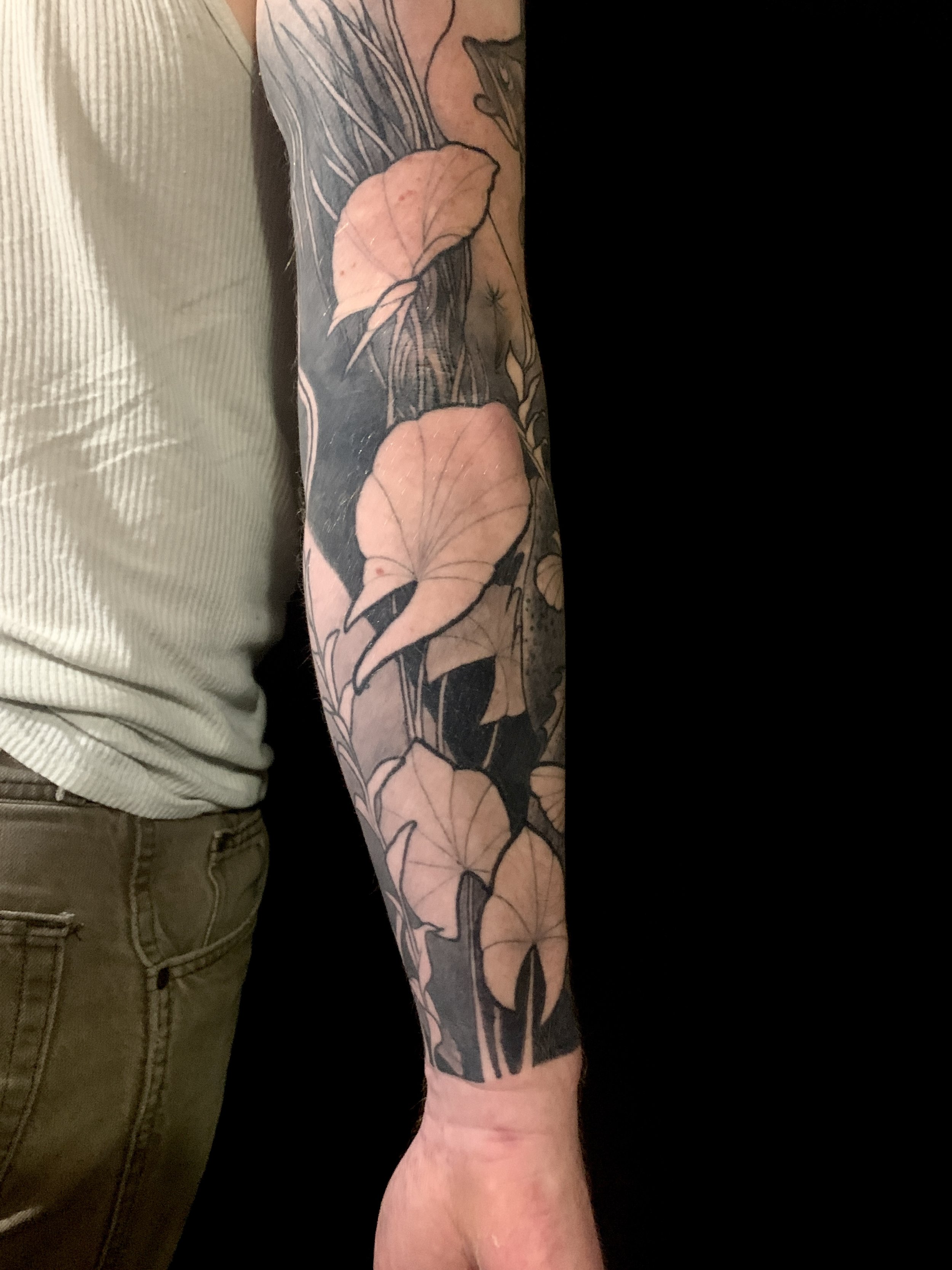 Tattoo of large leaves covered with black ink on a person's arm.