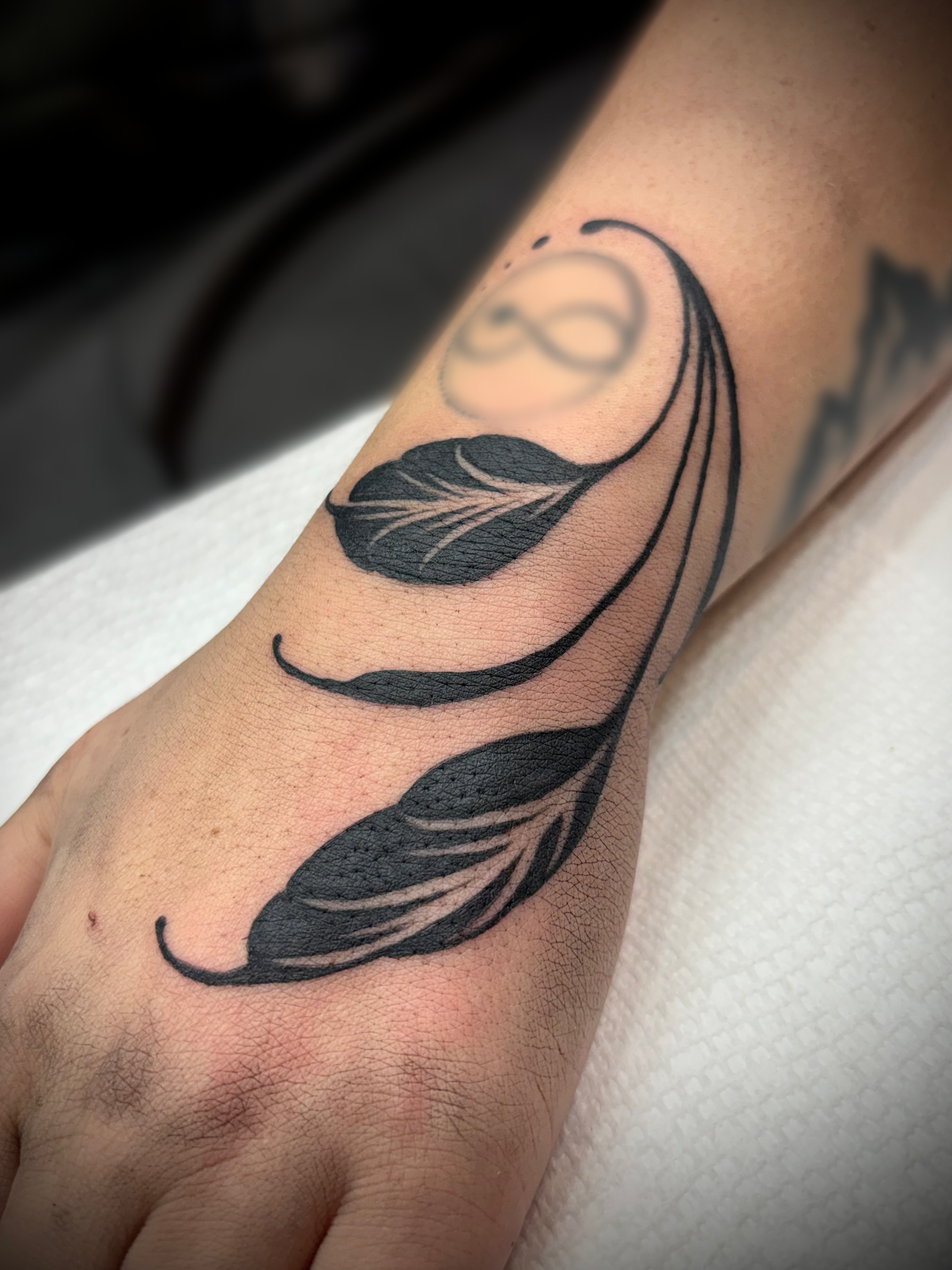 Tattoo of a moon, leaves, and an infinity symbol on a person's inner forearm.